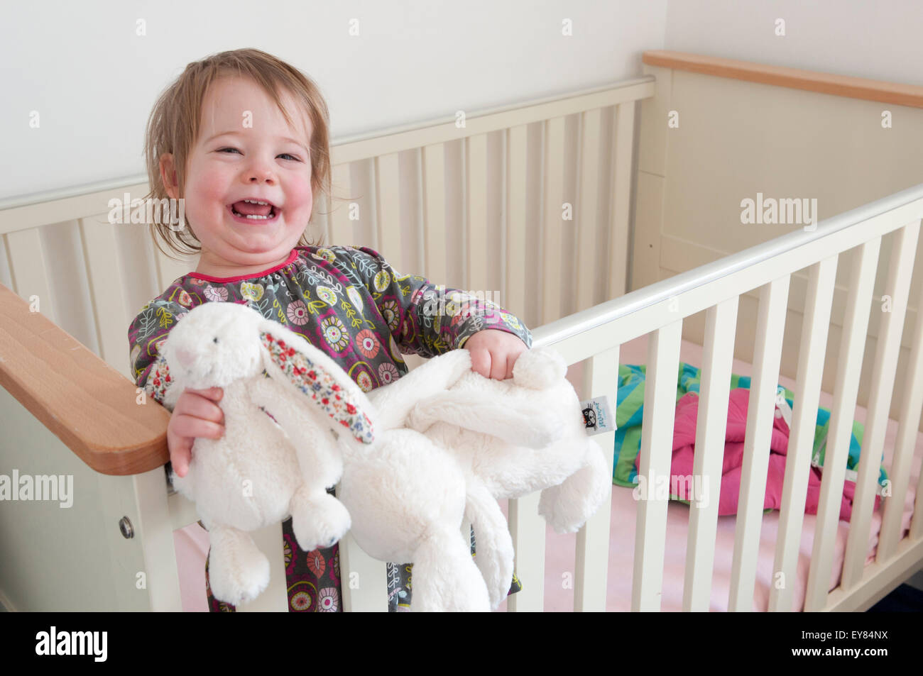 Felice bambina in piedi nella sua culla a giocare con i giocattoli morbidi Foto Stock