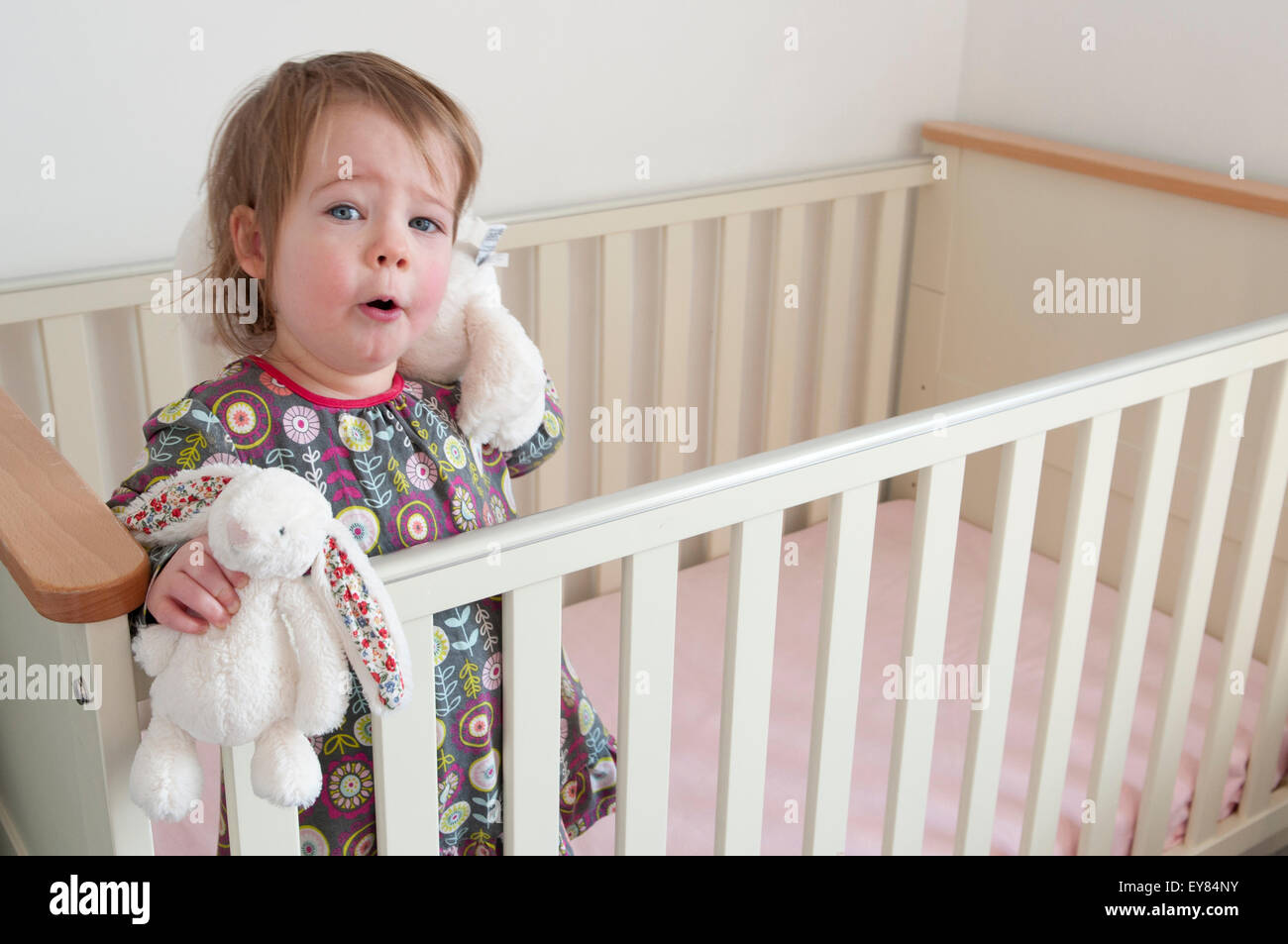 Felice bambina in piedi nella sua culla a giocare con i giocattoli morbidi Foto Stock