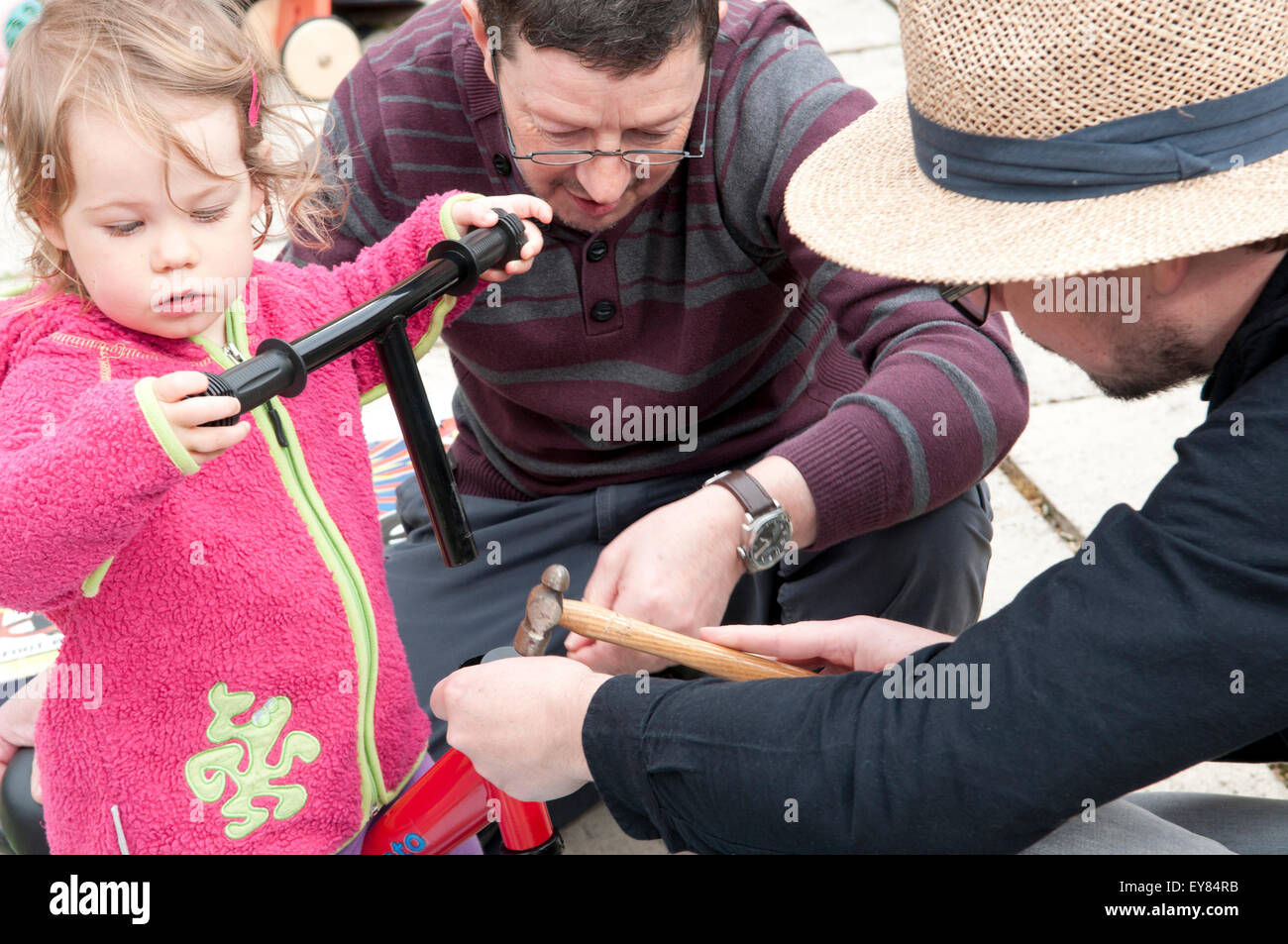 Bambina aiutando il suo nonno e papà assemblare il suo equilibrio rosso bike Foto Stock