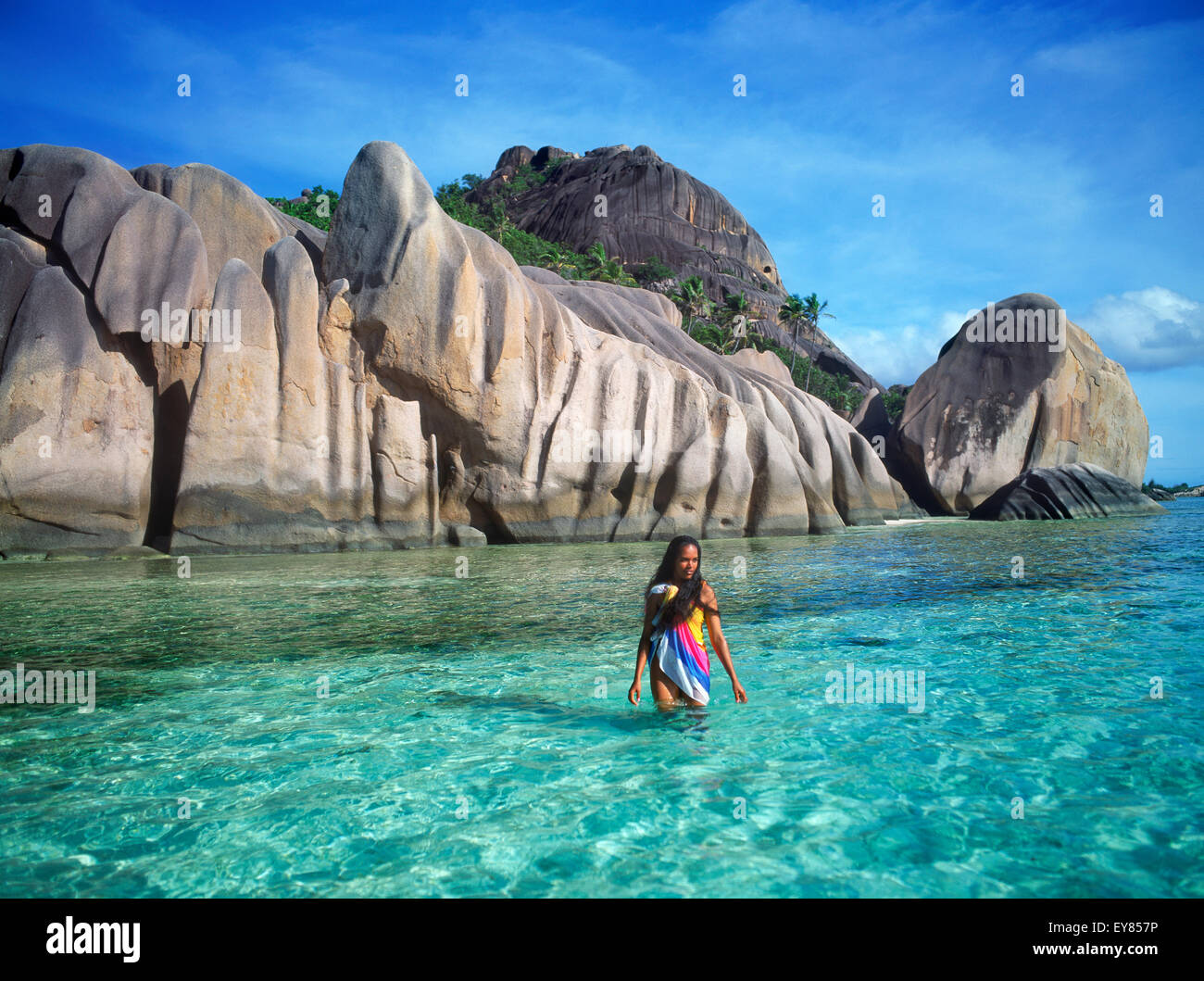Donna nativa con colorati sarong camminare in acque aqua ad Anse Source d Argent su La Digue alle Seychelles Foto Stock