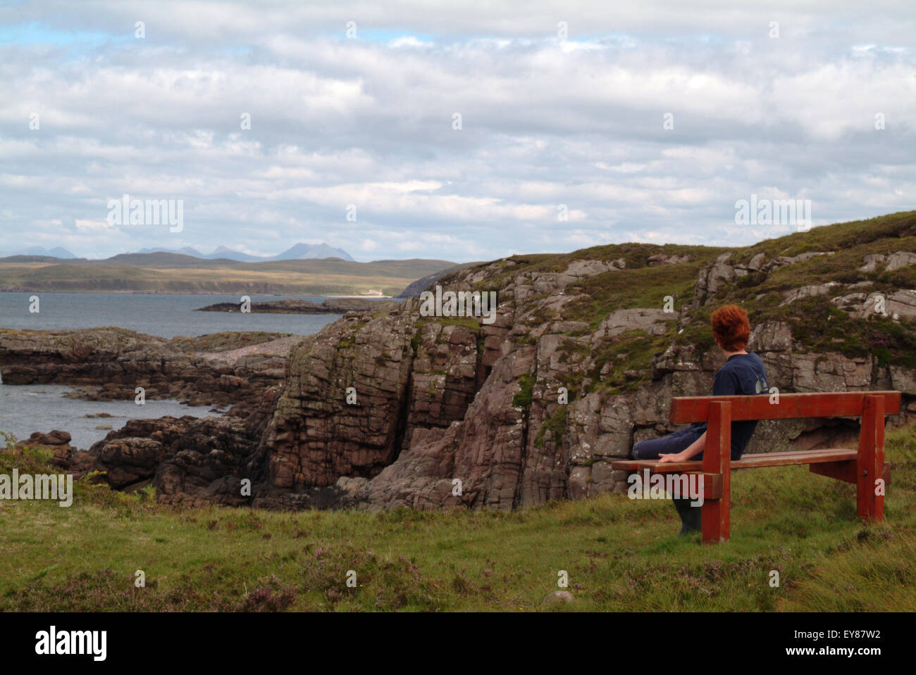 Ragazzo adolescente seduto su una panca di legno che guarda verso il mare Foto Stock