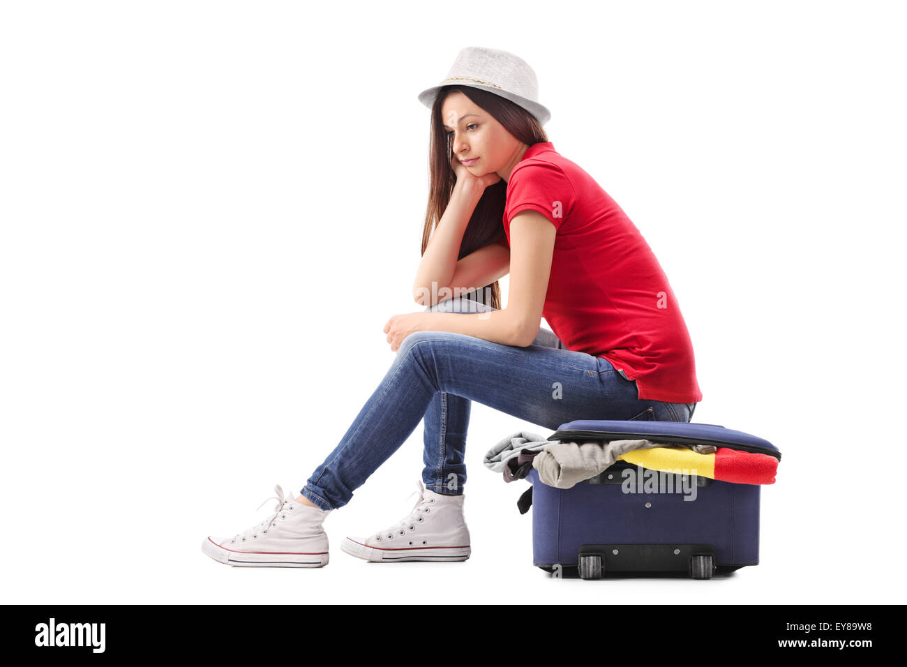 Triste giovane ragazza seduta su una valigia piena di abiti e di pensiero isolato su sfondo bianco Foto Stock