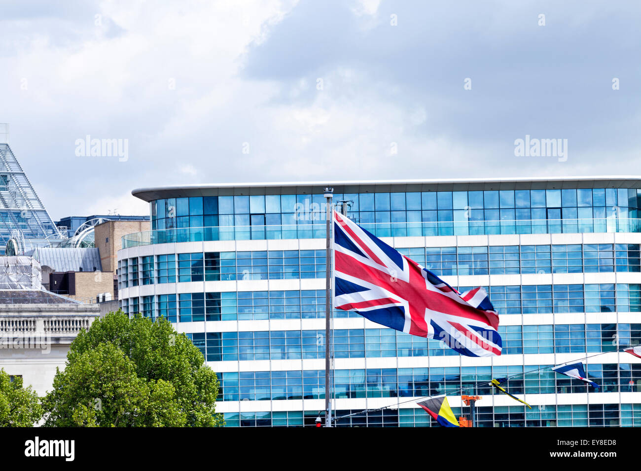Sventolare nel vento Unione Britannica bandiera di fronte a una finestra di vetro moderno edificio per uffici a Londra in un giorno nuvoloso Foto Stock