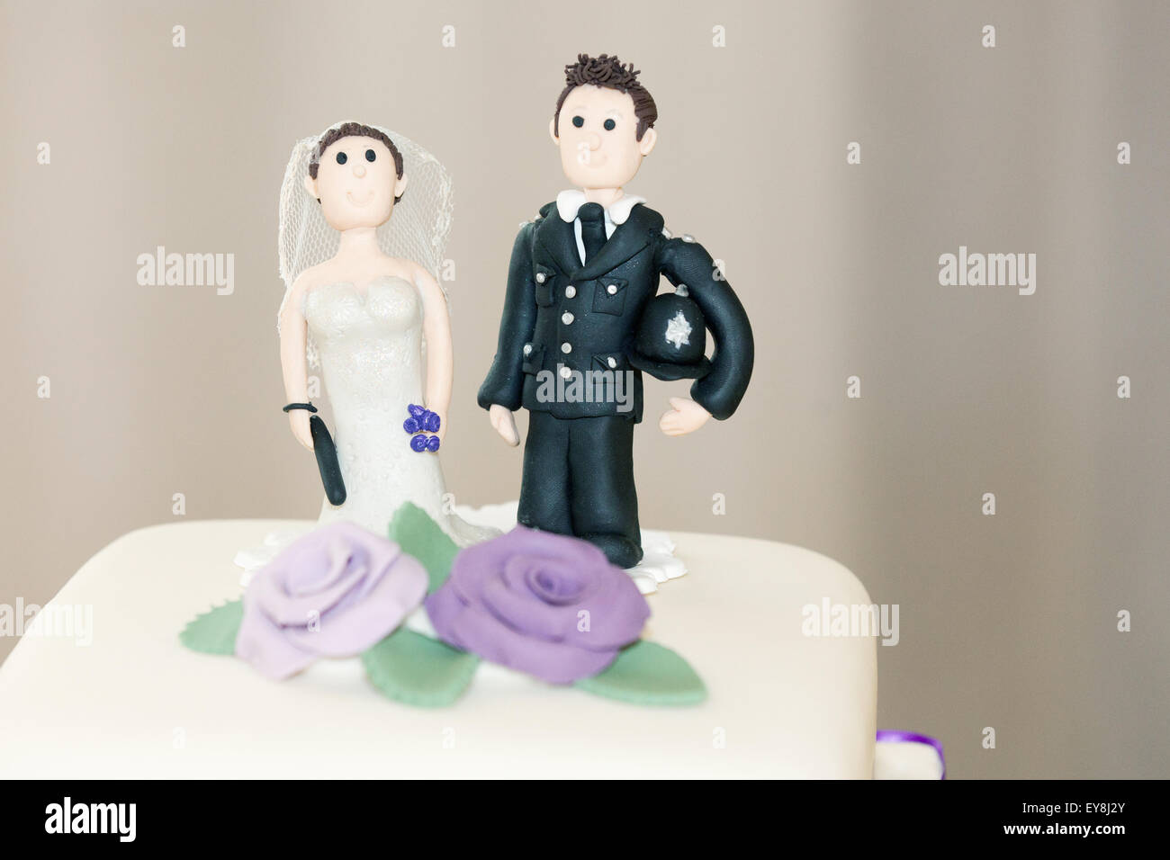 Un poliziotto divertente e il suo topper per torta da sposa, fatti a mano per una torta di nozze di coppia durante una cerimonia di nozze inglese. il poliziotto sta tenendo il suo casco Foto Stock
