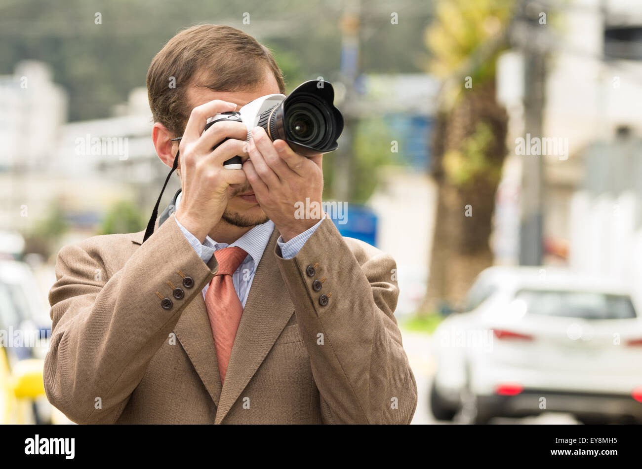 Successo maschio attraente fotografo indossare tuta marrone per lavorare in esterno nel traffico urbano tenere la fotocamera Foto Stock
