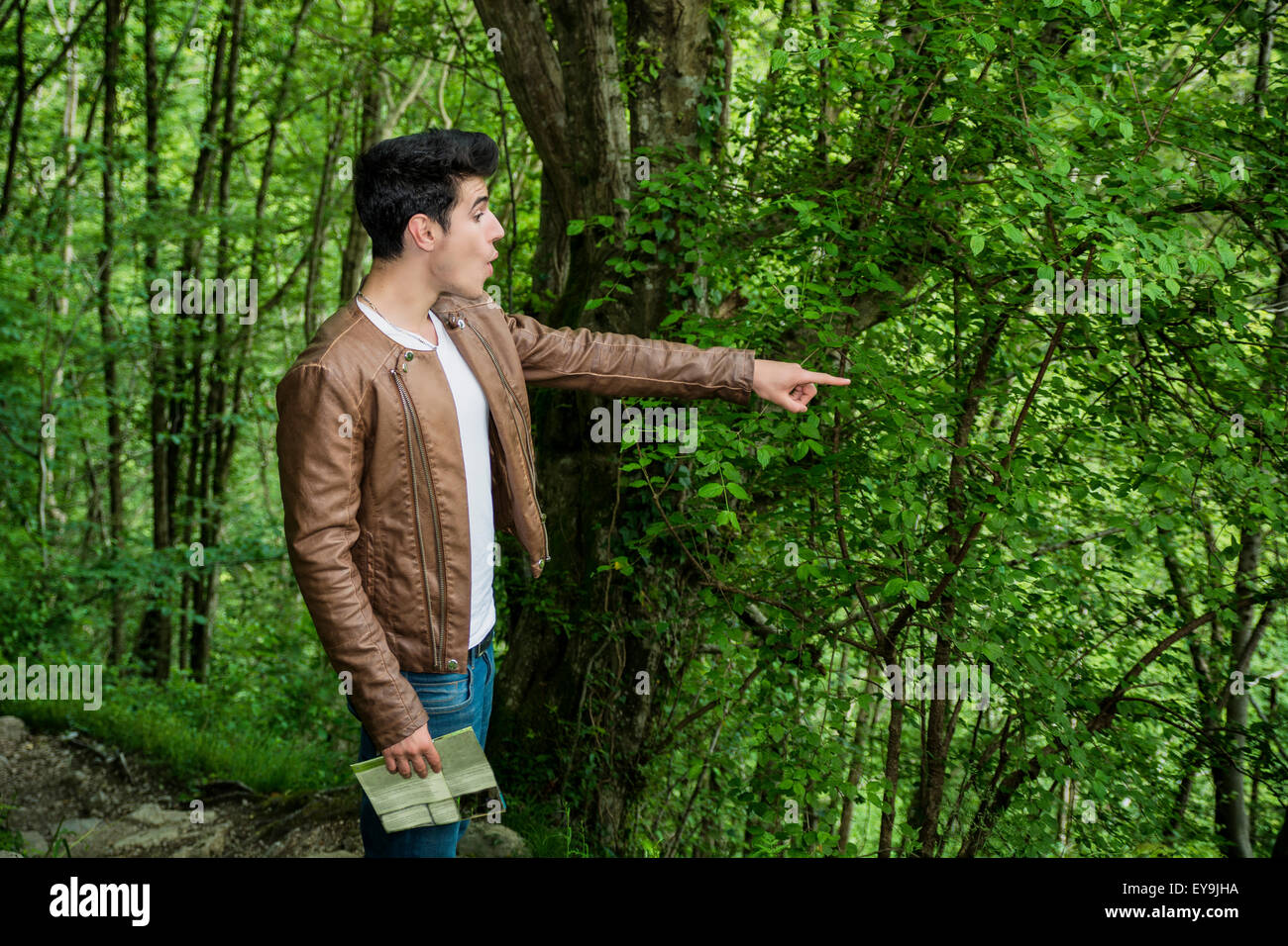 Stupito Cerca giovane uomo rivolto verso la distanza in zona boscosa, guardando qualcosa di stupefacente mentre sulla passeggiata attraverso la foresta Foto Stock