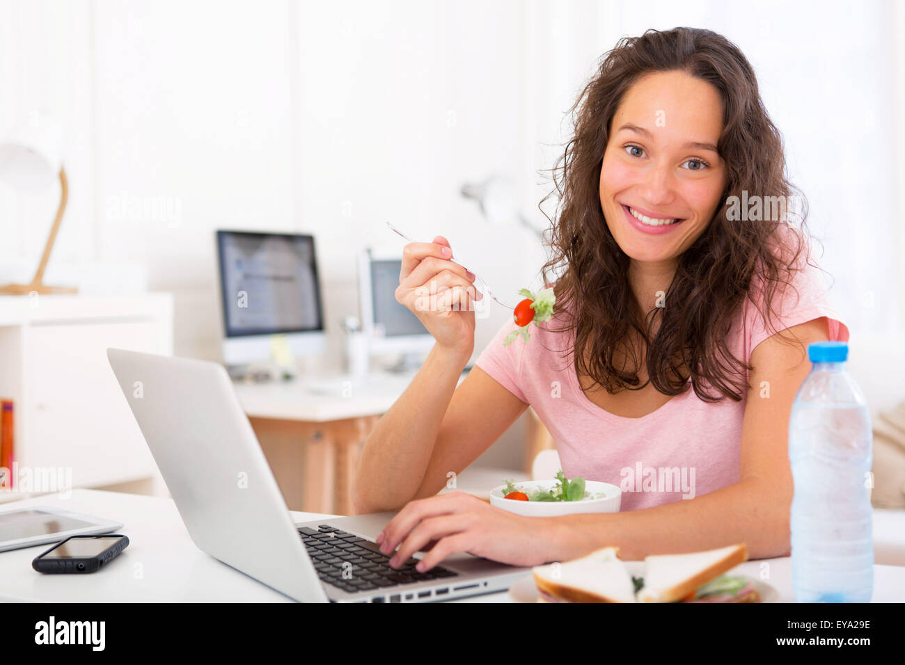 Vista di un giovane studente attraente insalata mangiare mentre si lavora Foto Stock