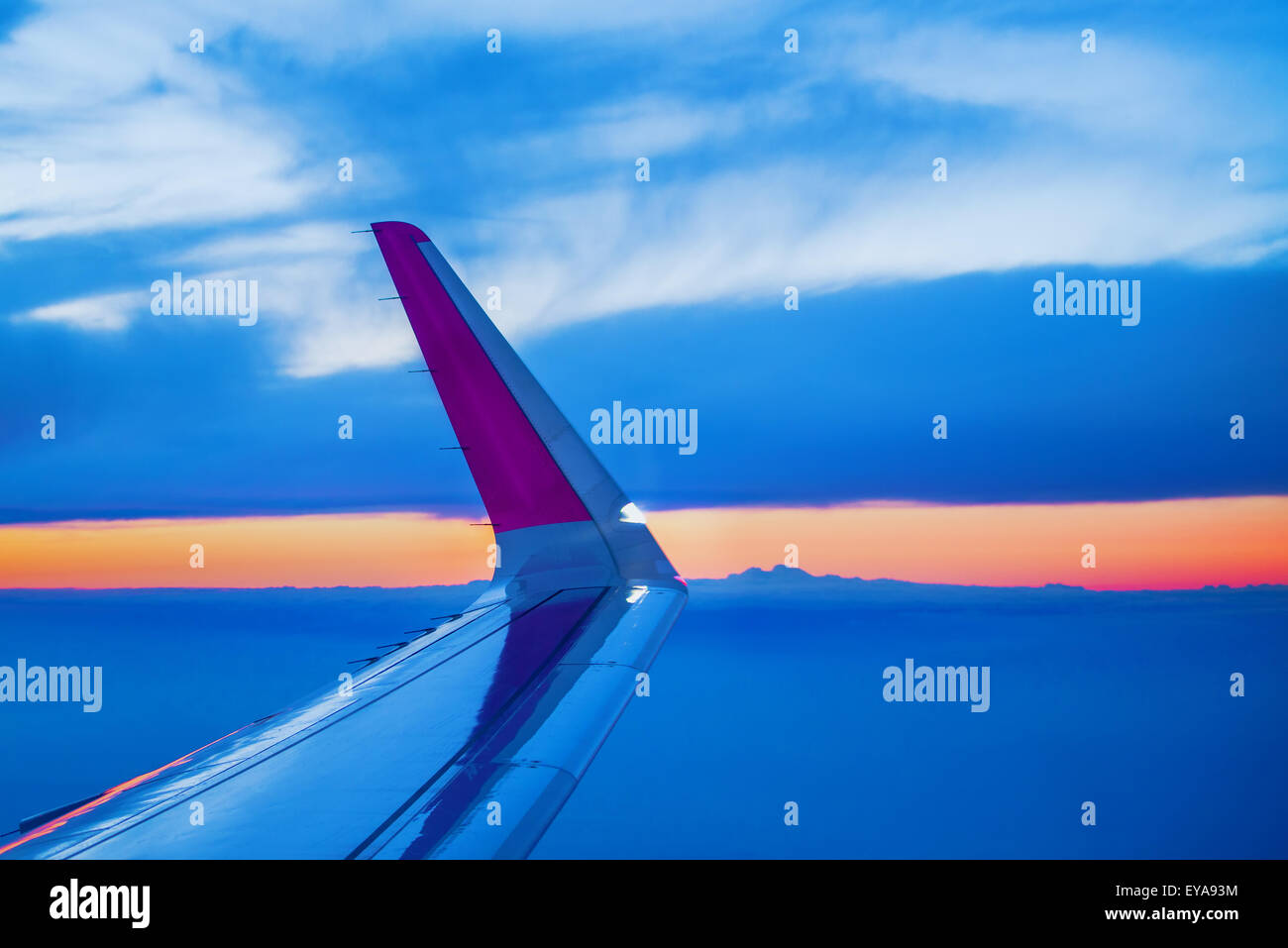 Ala di aeroplano visto attraverso oblò aperto finestrino durante il volo di gli aerei commerciali da trasporto passeggeri, tramonto sull'orizzonte Foto Stock