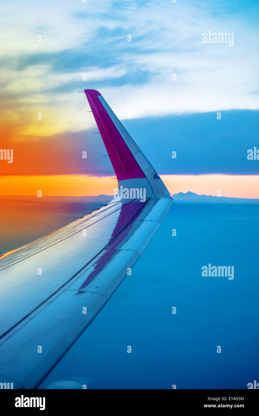 Ala di aeroplano visto attraverso oblò aperto finestrino durante il volo di gli aerei commerciali da trasporto passeggeri, tramonto sull'orizzonte Foto Stock