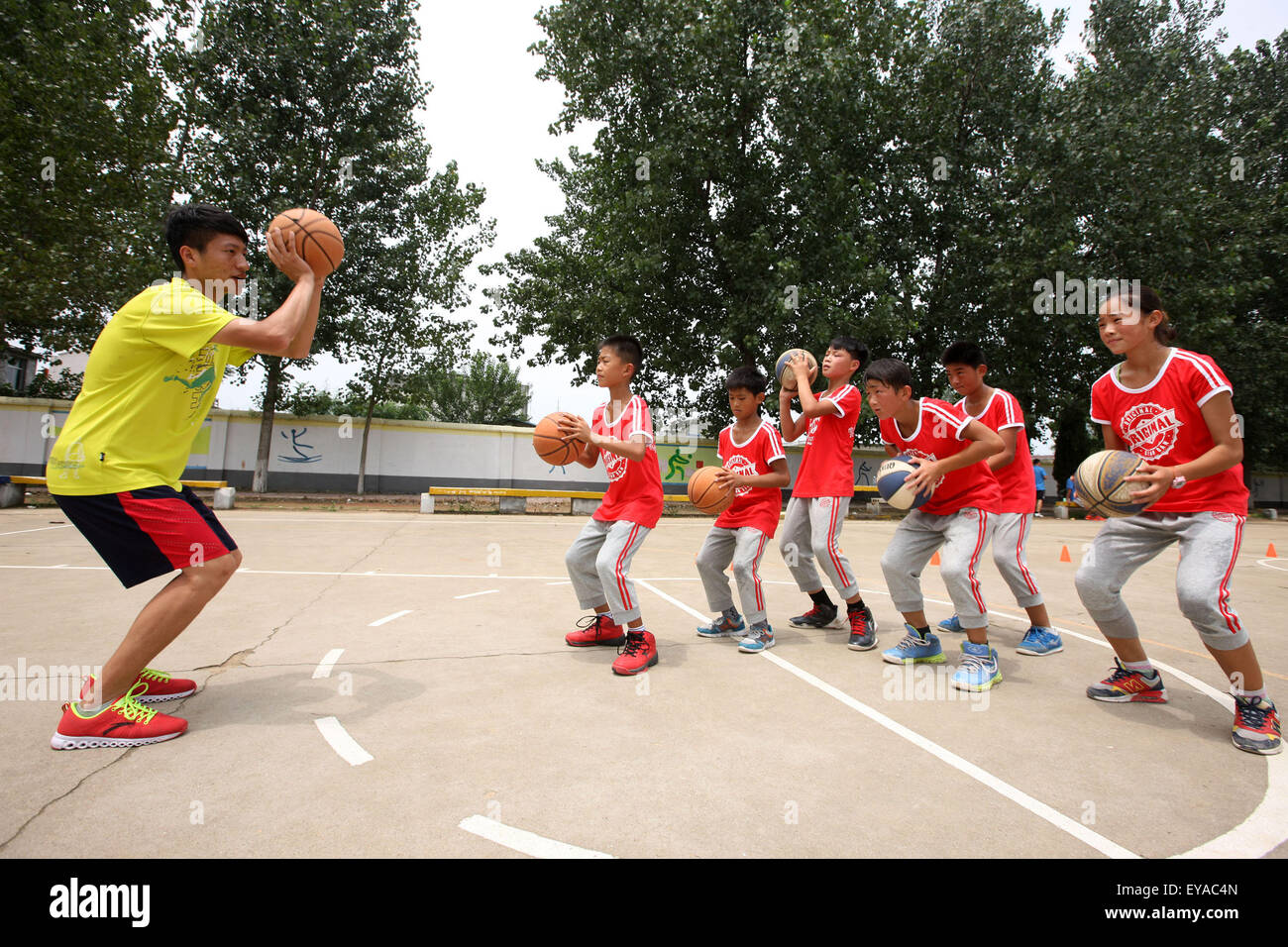 Bozhou, cinese della provincia di Anhui. Il 24 luglio, 2015. Uno studente di college (L) da Hefei normale università insegna a sinistra dietro i bambini come passare le palline in un gioco di basket in Mengcheng contea di Bozhou City, est cinese della provincia di Anhui, 24 luglio 2015. Bambini in diverse parti della Cina ha trascorso le vacanze estive in vari modi. © Hu Weiguo/Xinhua/Alamy Live News Foto Stock