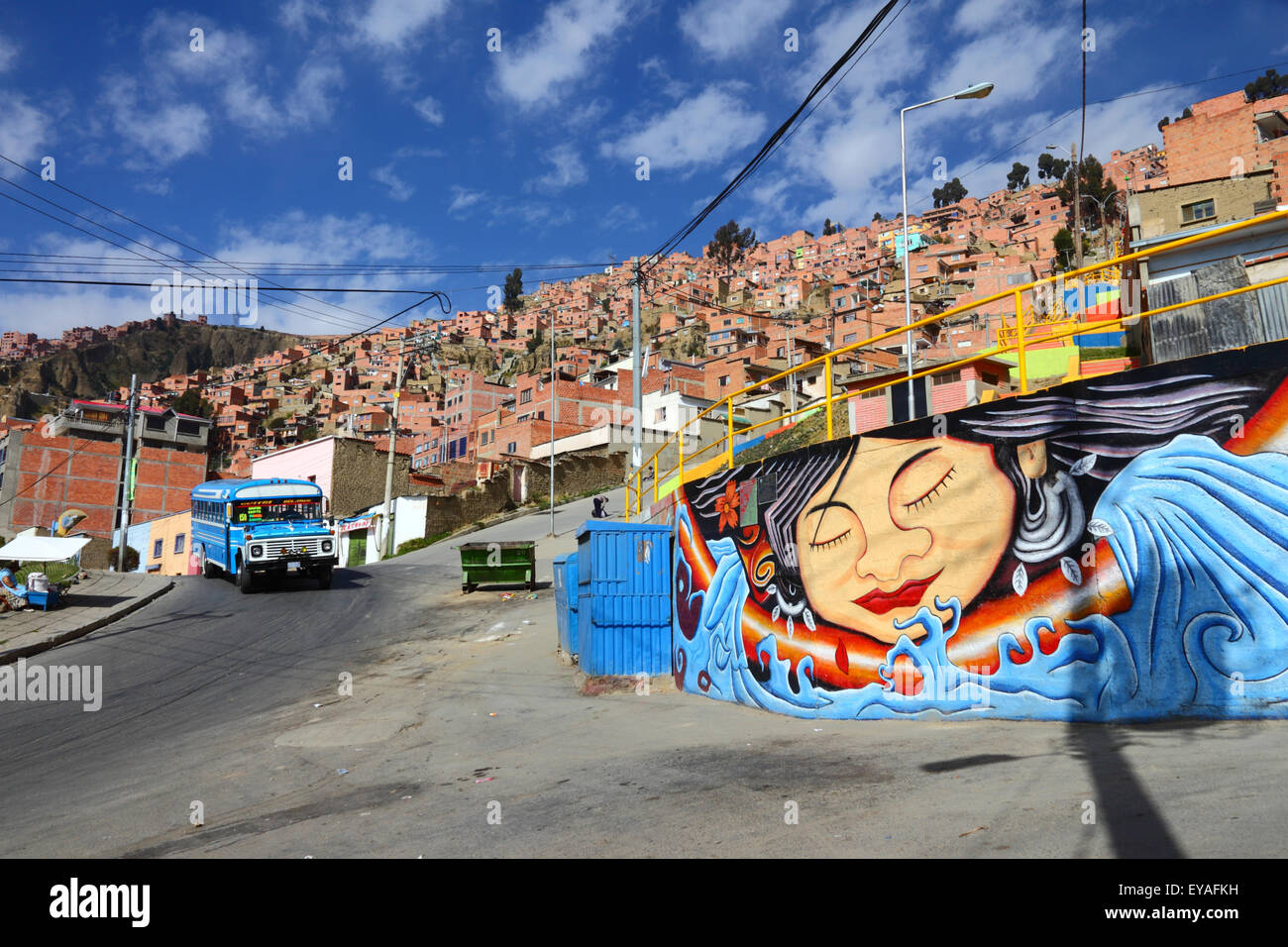 Murale su muro nel sobborgo della città su ripida collina, tipico vecchio micro bus blu utilizzato come trasporto pubblico in background, la Paz, Bolivia Foto Stock