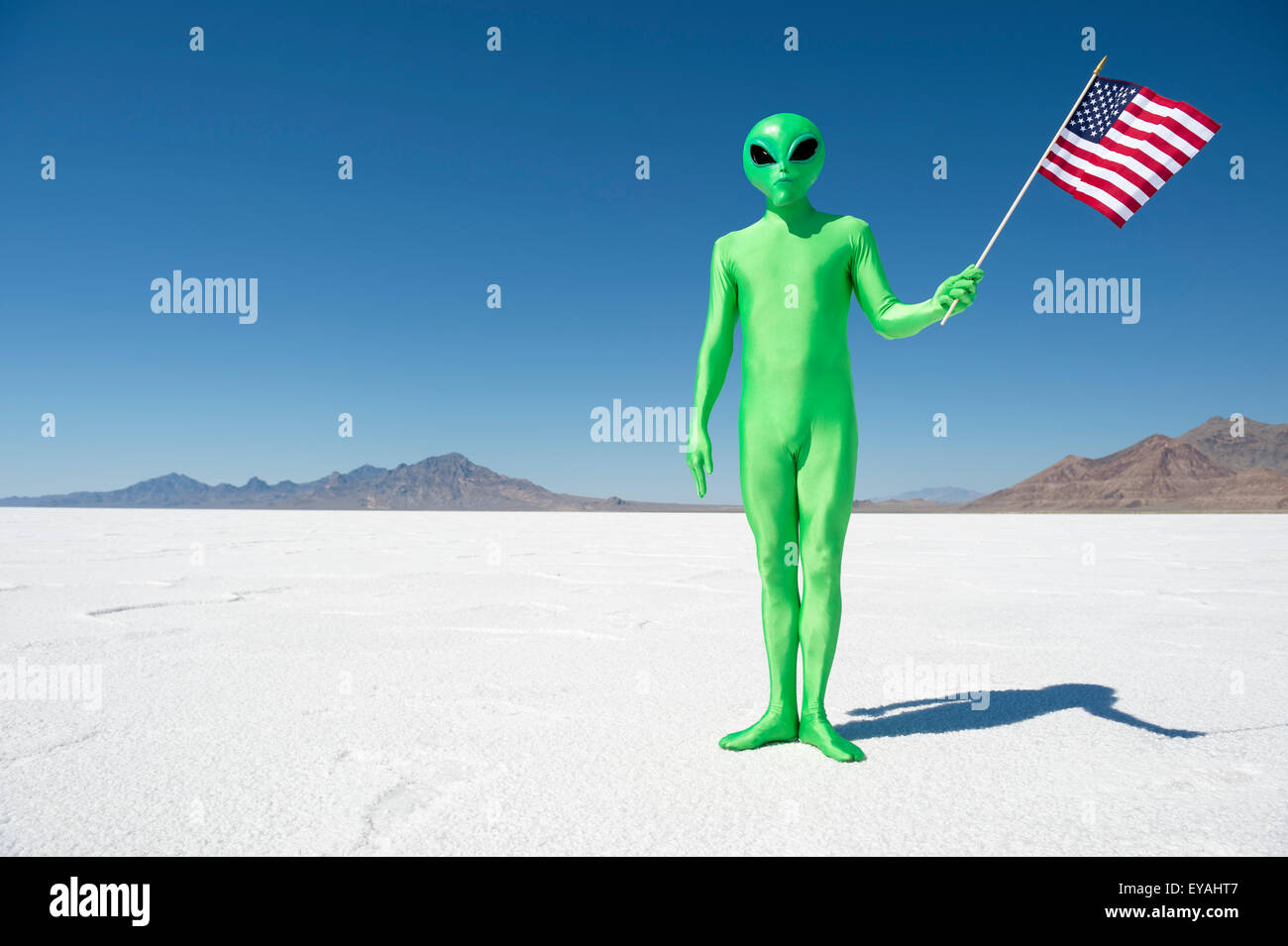 (Legale o illegale) alien facendo una patriottica dichiarazione di immigrazione tenendo una bandiera americana sul drammatico paesaggio lunare Foto Stock