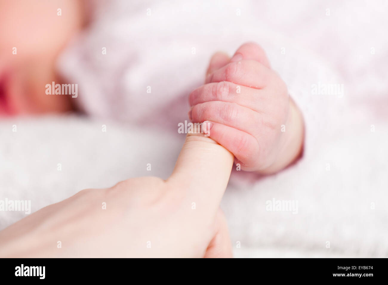 Un giovanissimo baby presa sulla sua madri dito che mostra la sua piccola chiodi sulla sua mano serrata. Il bambino sfocata è addormentato in background Foto Stock