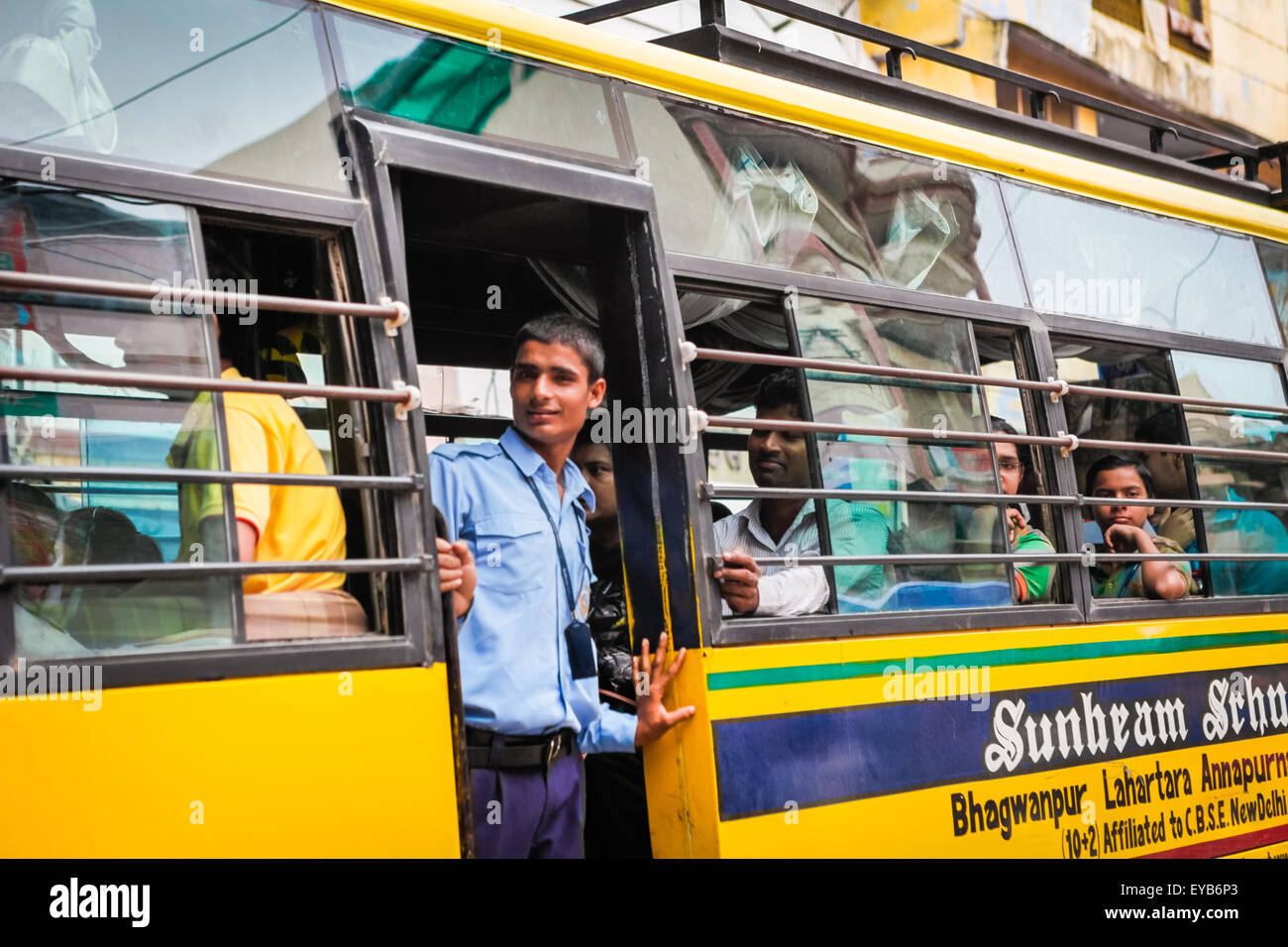 Uno studente che guarda fuori dalla porta d'ingresso di un bus scolastico che si muove su una strada trafficata a Varanasi, Uttar Pradesh, India. Foto Stock