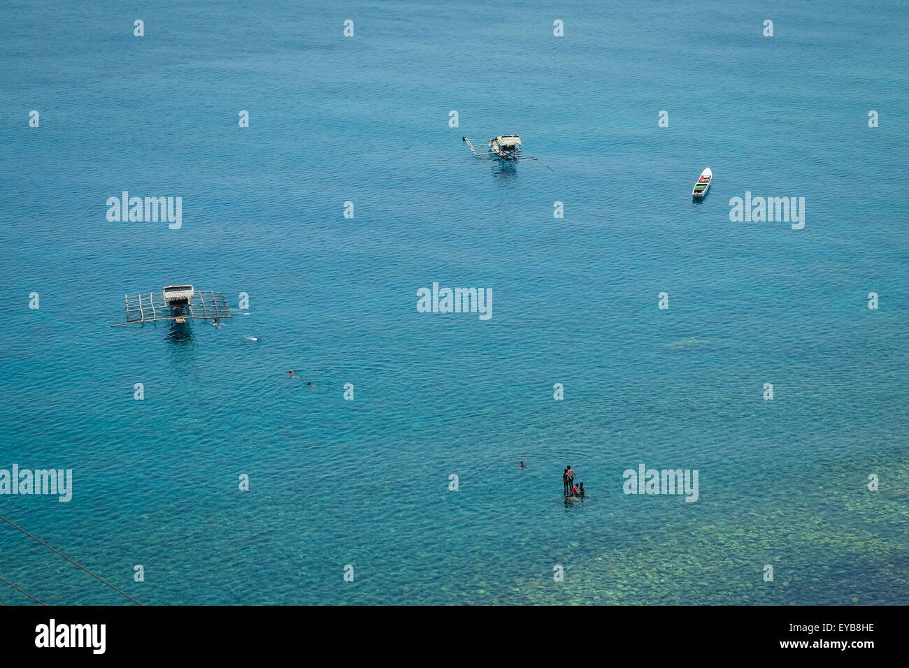 Allevamenti di pesci, barche e bambini sulle acque costiere sono visti da una collina costiera a Lamagute, Lembata, Nusa Tenggara orientale, Indonesia. Foto Stock