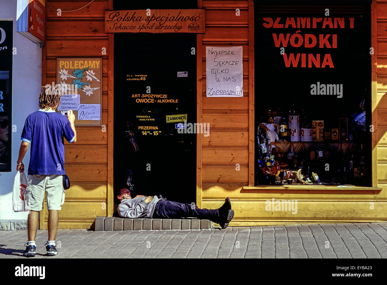 Un pedone prende una fotografia di un uomo dorme nella porta di una vodka store. Zakopane. La Polonia. Foto Stock