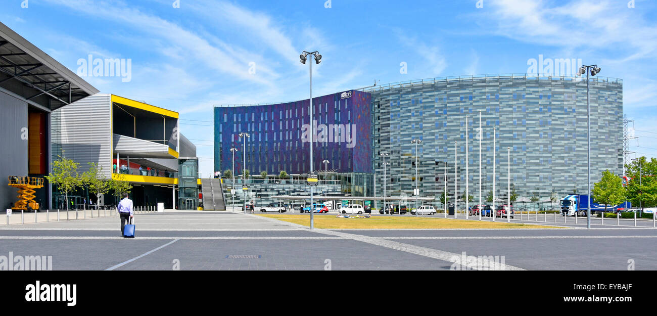 Uomo d'affari che cammina verso l'entrata orientale del centro esposizioni Excel di Londra giallo & adiacente moderno Aloft W hotel London Docklands Inghilterra Regno Unito Foto Stock