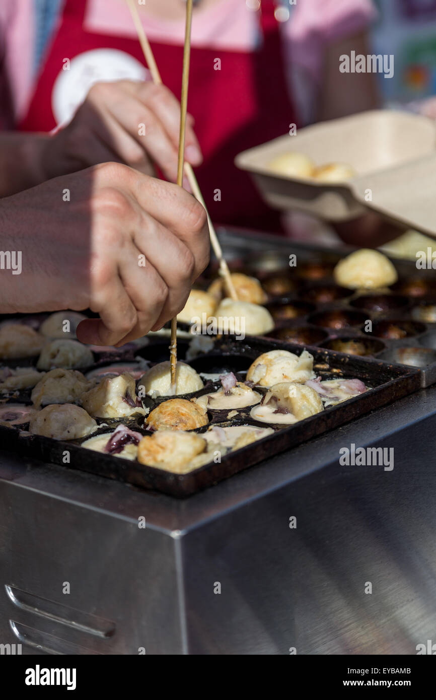 La cottura di hot takoyaki sfere nella cucina di strada con la gente le mani Foto Stock