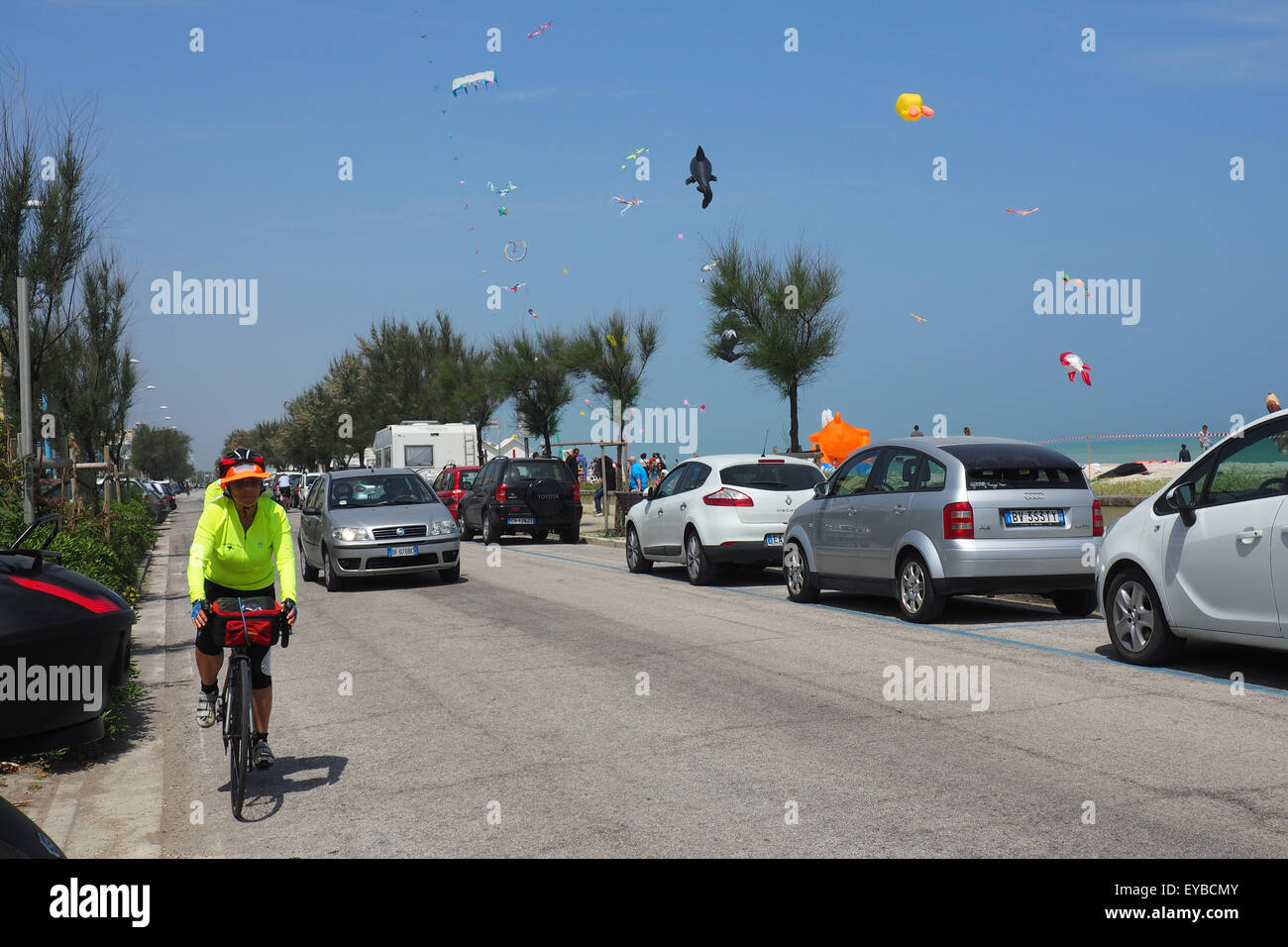 Cicloturisti a cavallo su una strada lungo una spiaggia dove aquiloni sono battenti. Foto Stock