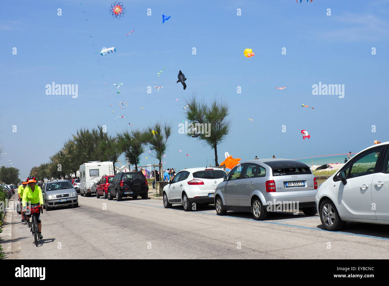 Cicloturisti a cavallo su una strada lungo una spiaggia dove aquiloni sono battenti. Foto Stock