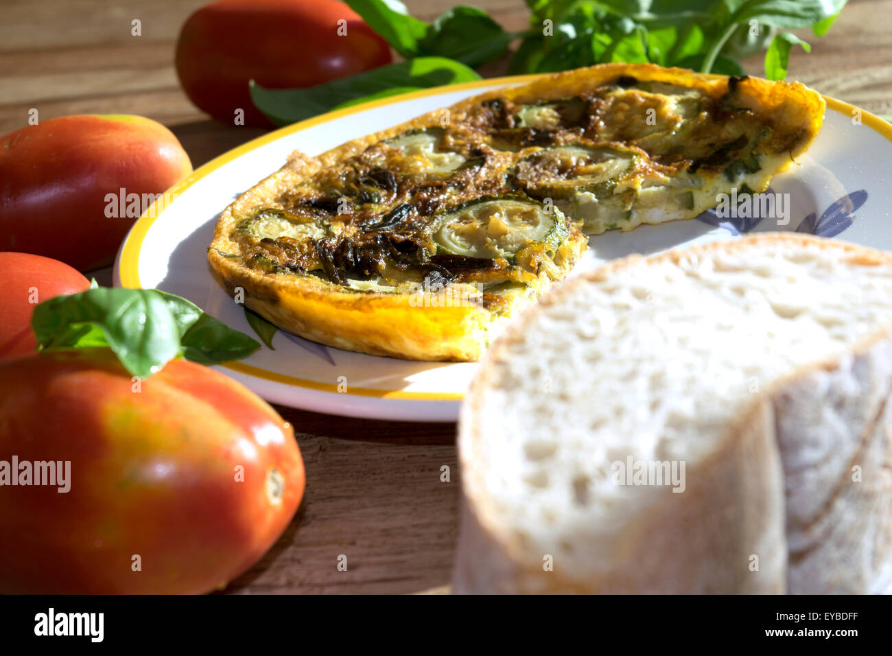 Frittata di zucchine su una tavola apparecchiata con un po' di pane e di altri ortaggi Foto Stock