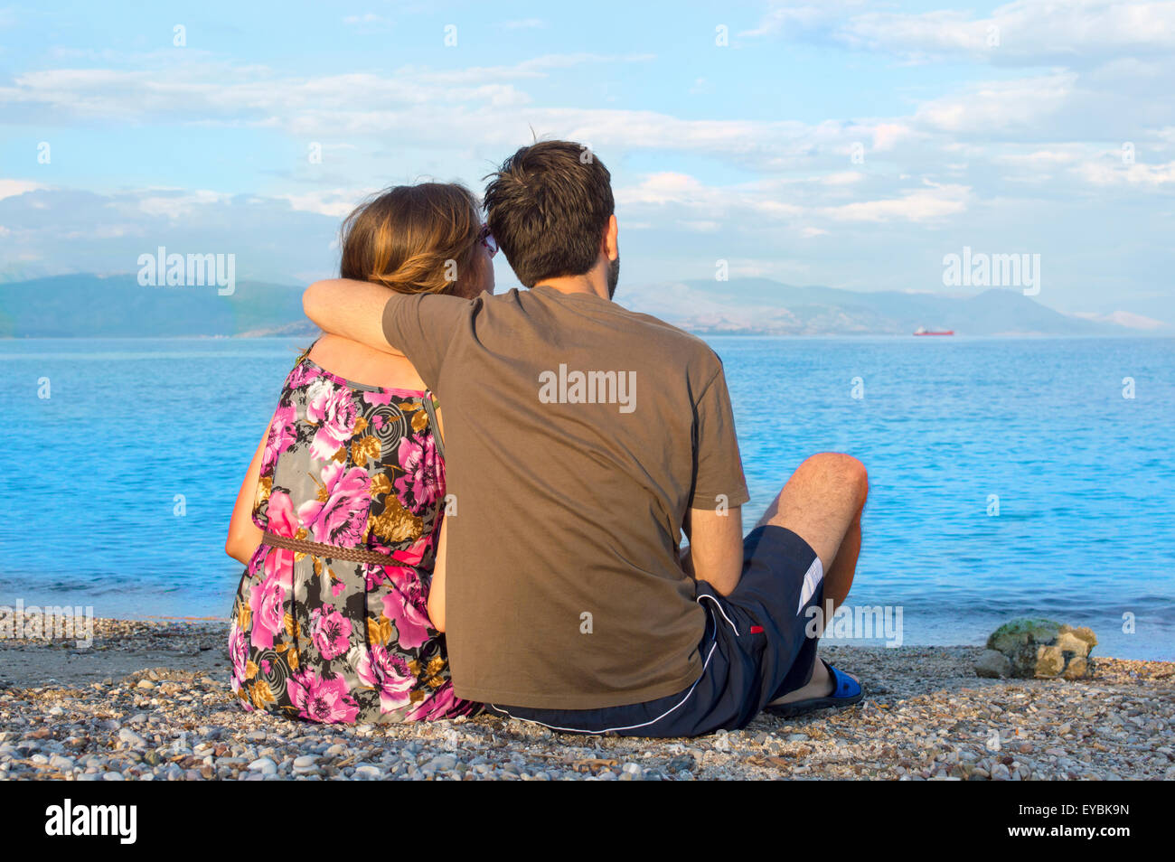 Giovani amare giovane seduti insieme su una spiaggia rocciosa e guardando il mare Foto Stock