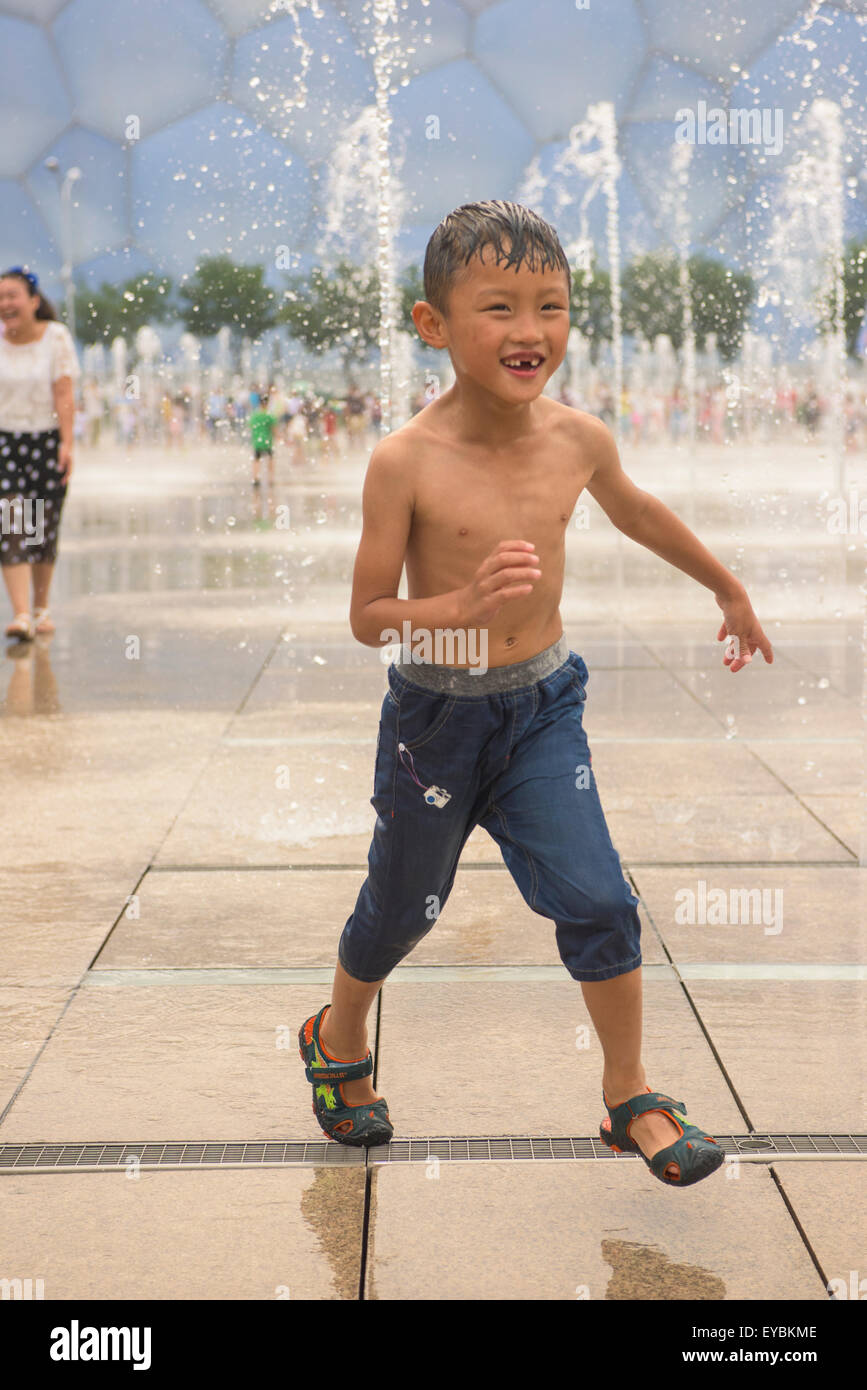 Il ragazzo si divertono tra l'acqua-sprinkler presso il Parco Olimpico di Pechino, Cina - Luglio 2015 Foto Stock