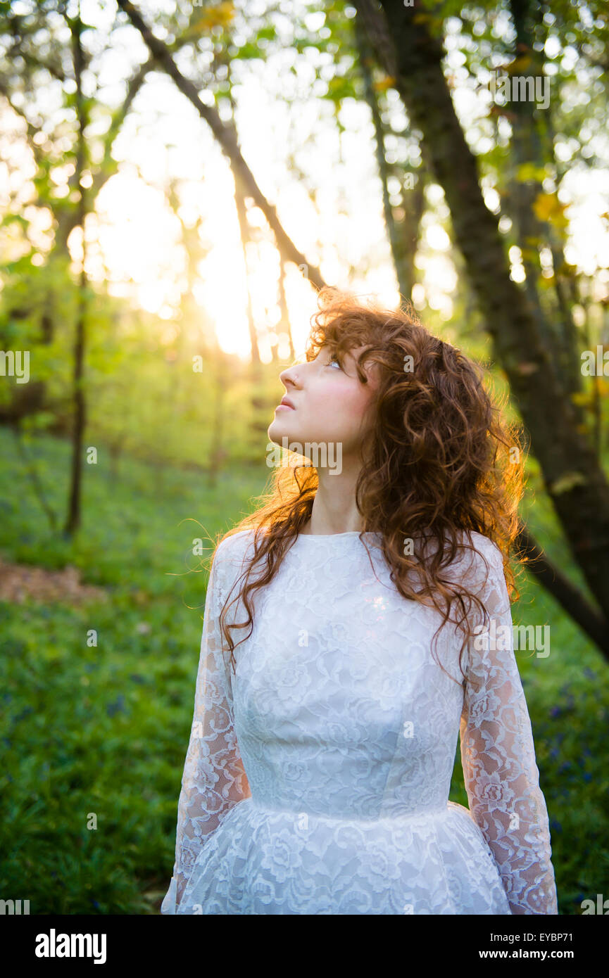 Runaway sposa: una sottile bruna giovane donna dai capelli indossando un bianco abito da sposa da soli in un bosco foresta, serata primaverile, REGNO UNITO Foto Stock