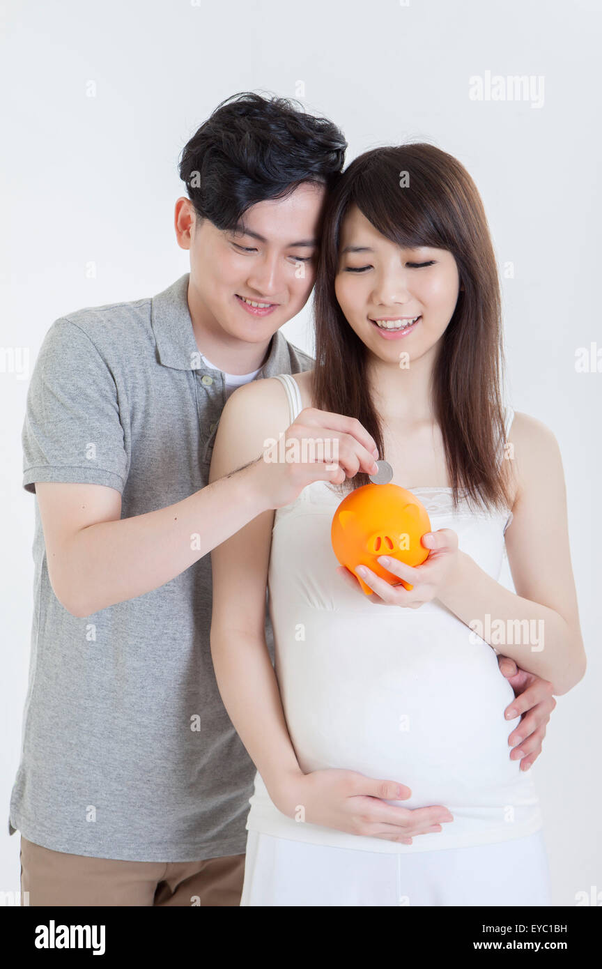 Giovane uomo e donna incinta holding salvadanaio insieme, Foto Stock
