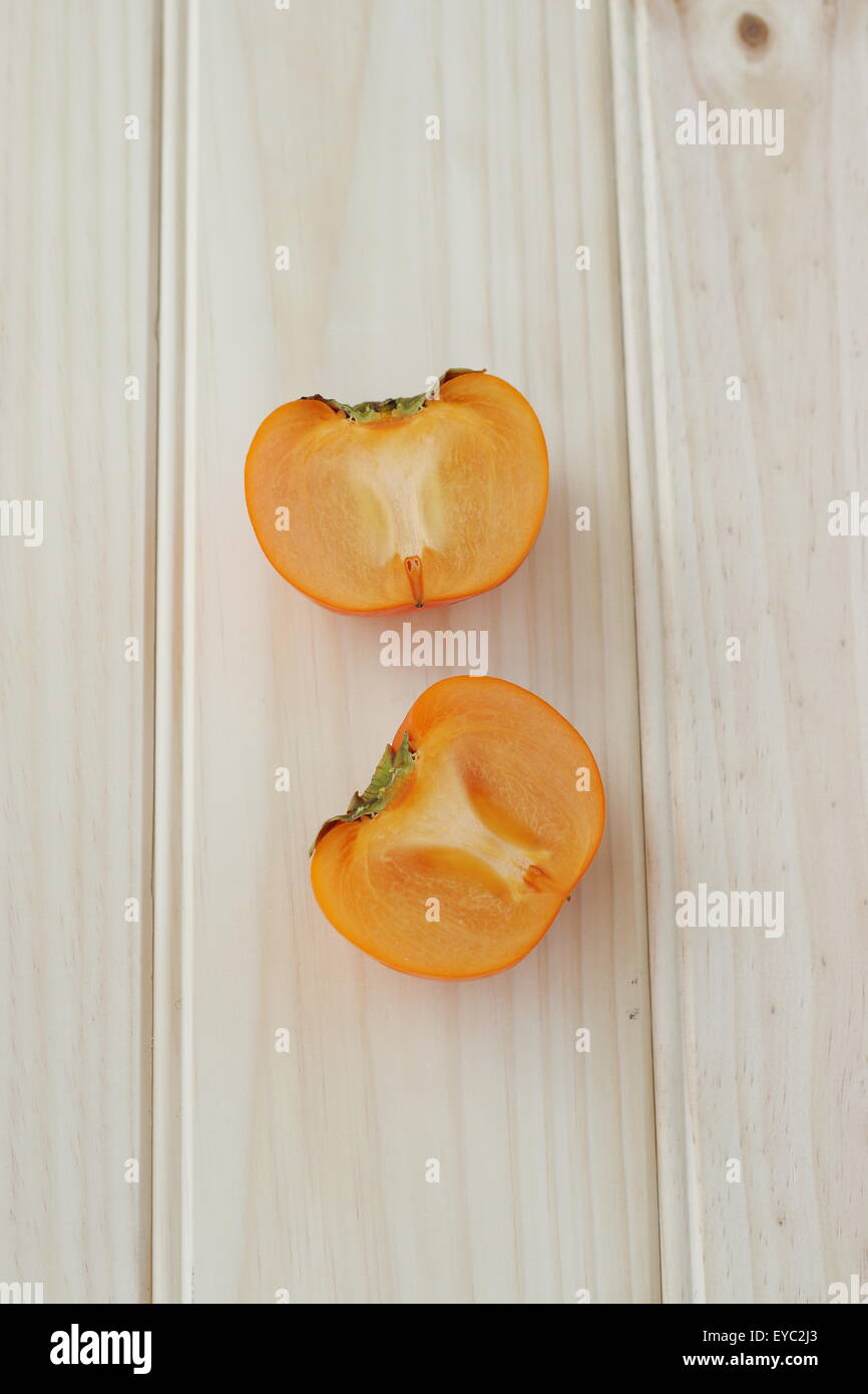 Uno fresco colore arancio kaki tagliato a metà su una tavola di legno Foto Stock