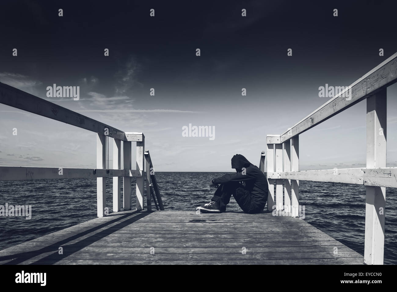 Da solo giovane uomo seduto a bordo del molo in legno - Disperazione, solitudine, il concetto di alienazione, in bianco e nero Foto Stock