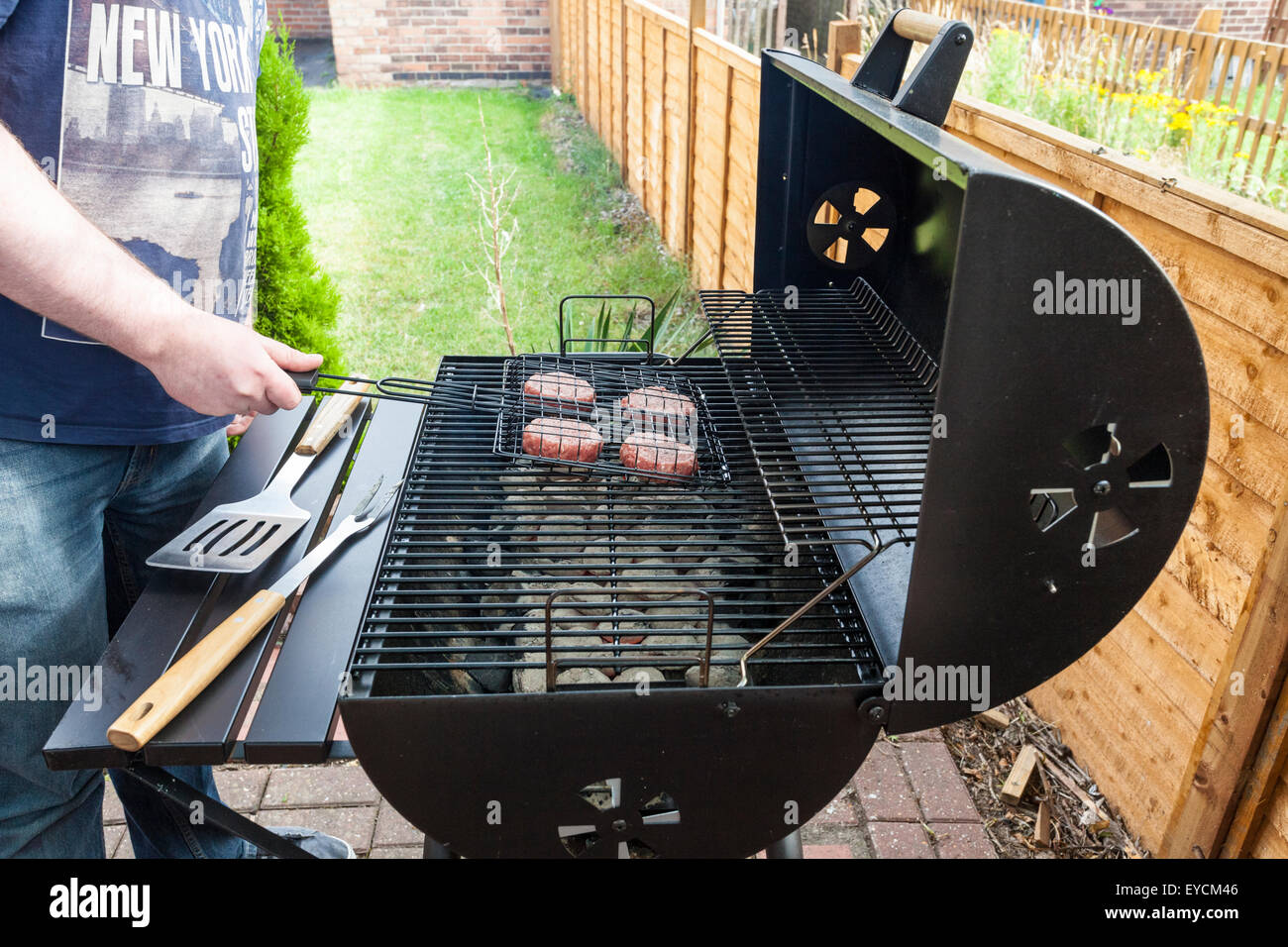 Barbecue a casa. L uomo alla brace hamburger su un barbecue nel giardino Foto Stock