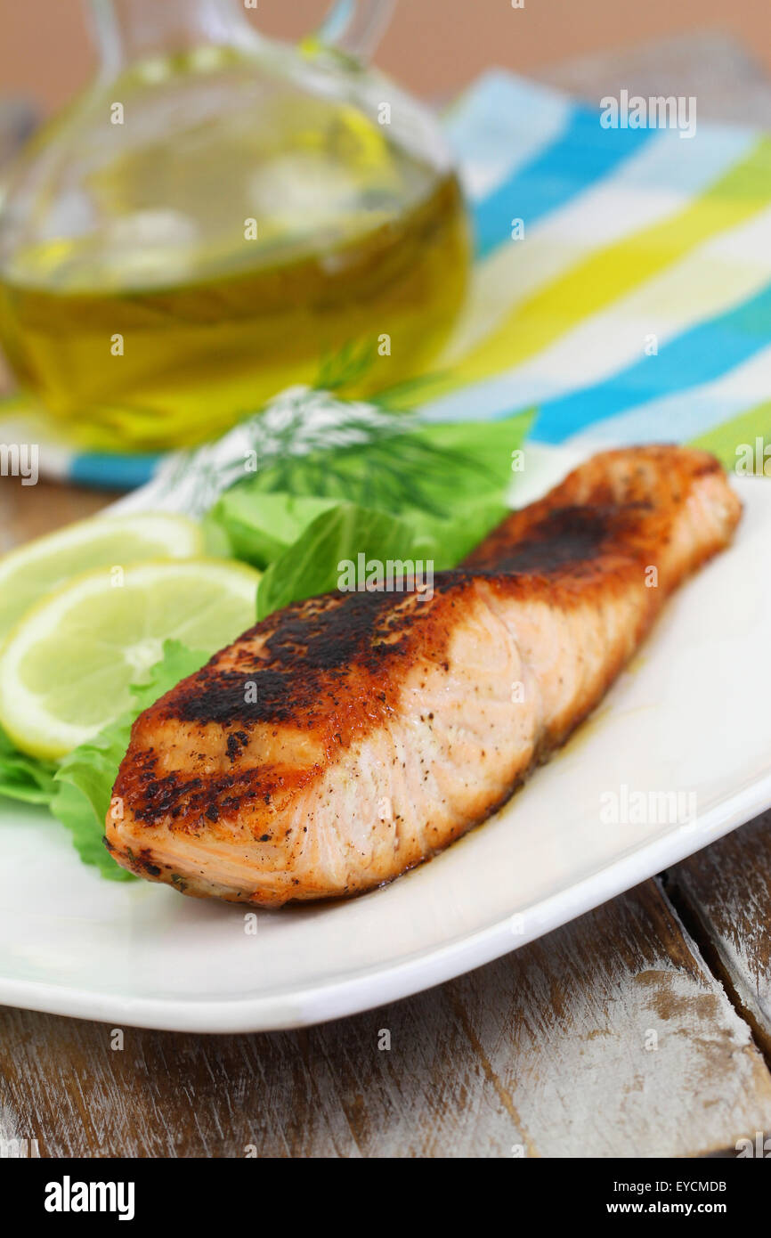 Salmone alla griglia sulla piastra bianca con insalata verde e limone, primo piano Foto Stock