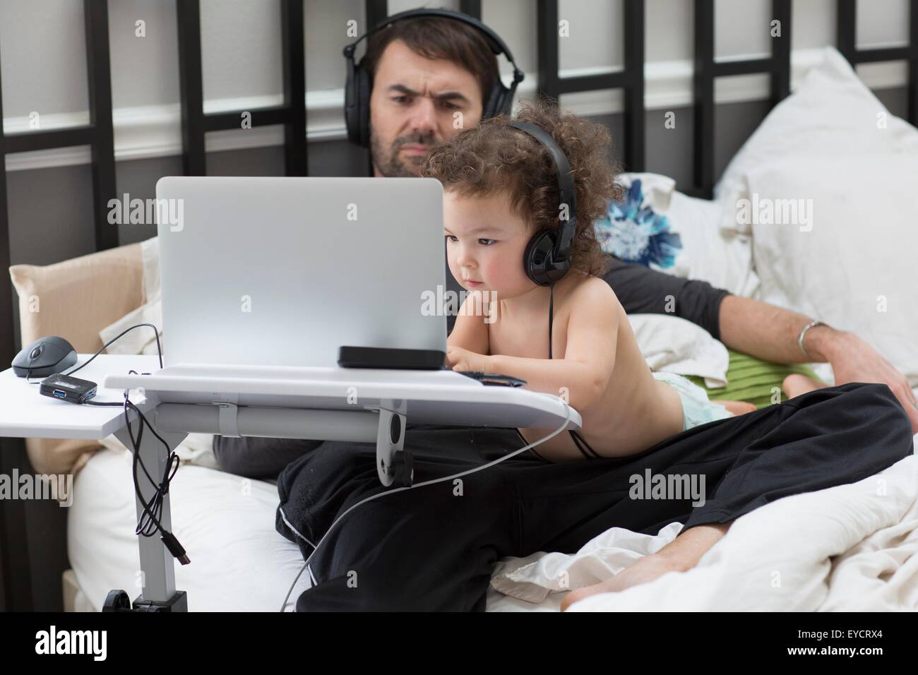 Padre guarda figlia toddler digitando su laptop a letto Foto Stock