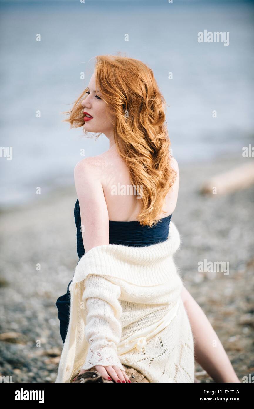 Giovane donna con lunghi capelli rossi guardando sopra la sua spalla sulla spiaggia, Bainbridge Island, nello Stato di Washington, USA Foto Stock