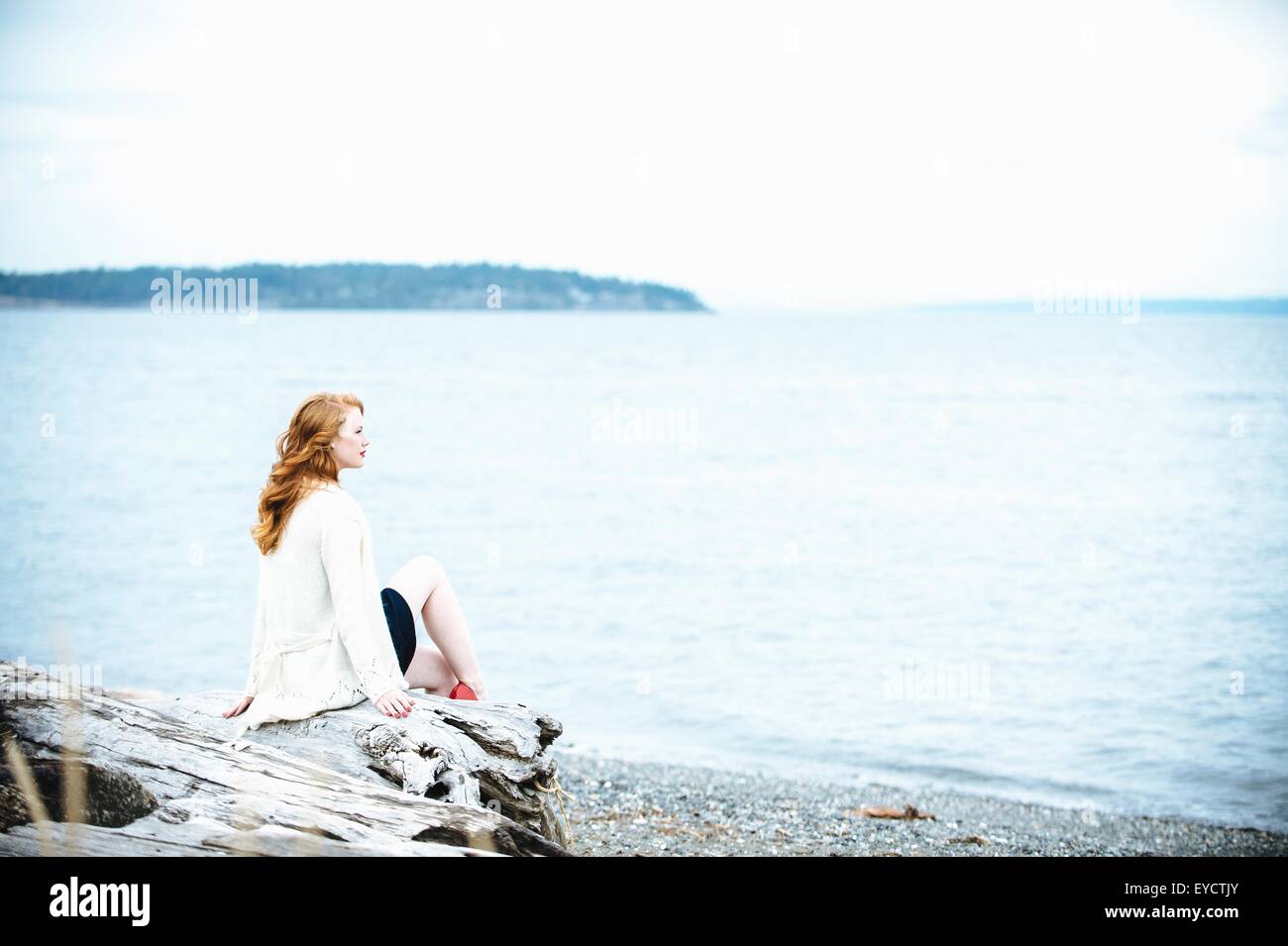 Giovane donna seduta sulla spiaggia che guarda al mare, Bainbridge Island, nello Stato di Washington, USA Foto Stock