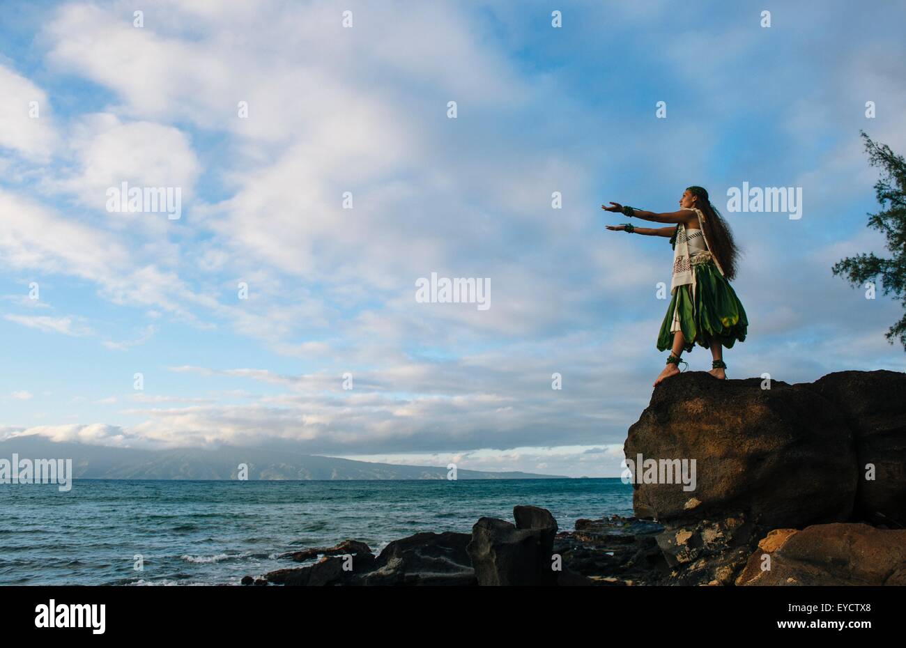 Donna hula sulla parte superiore delle rocce costiere indossando il costume tradizionale, Maui, Hawaii, STATI UNITI D'AMERICA Foto Stock