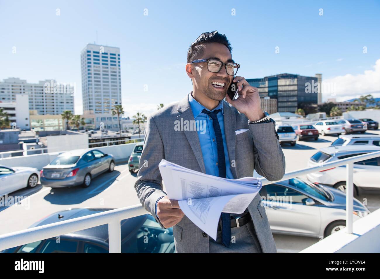 Giovane imprenditore sul tetto della città parcheggio auto a sorridere mentre parli sullo smartphone Foto Stock