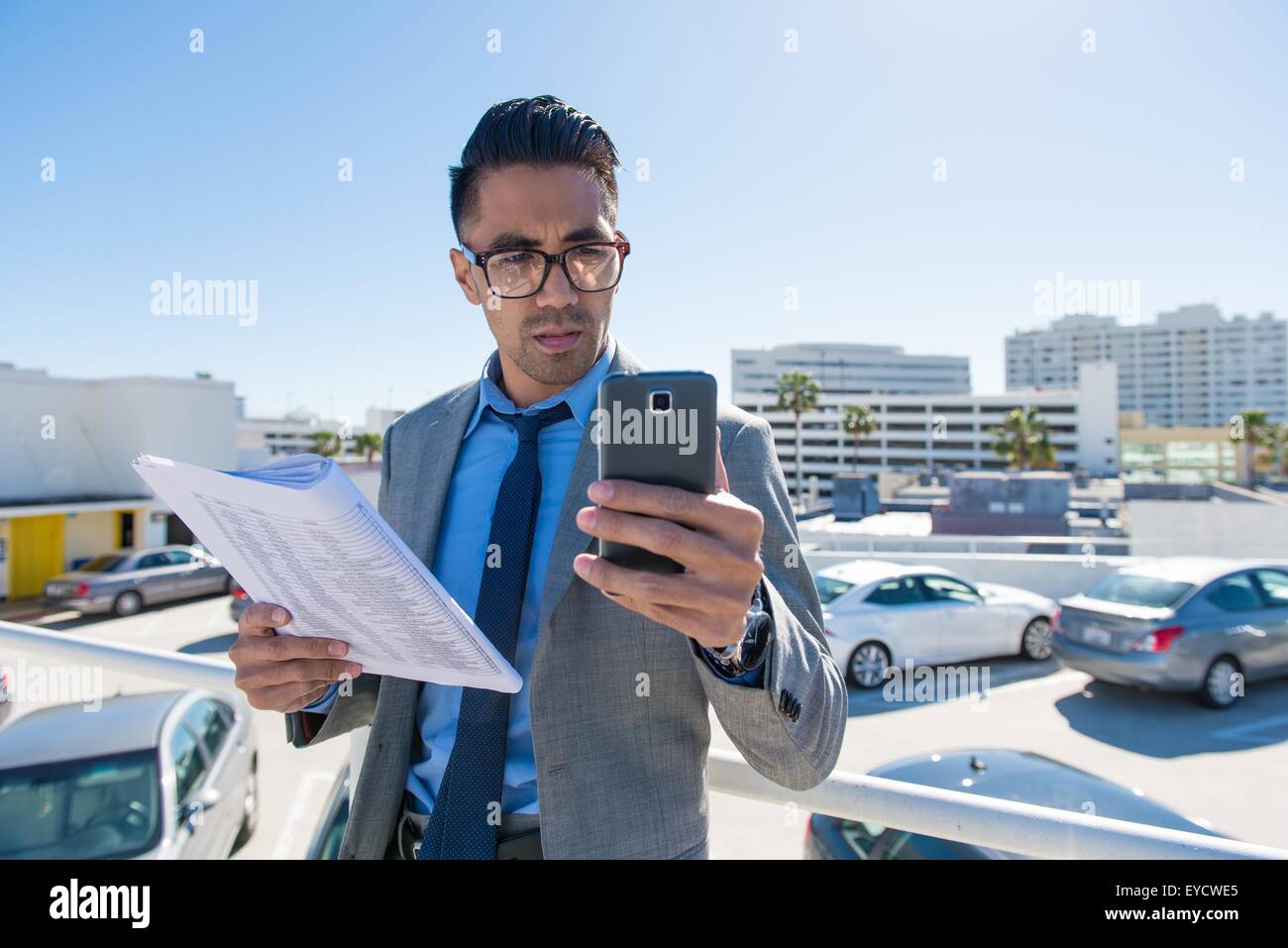 Giovane imprenditore sul tetto della città parcheggio auto la lettura di testi dello smartphone Foto Stock