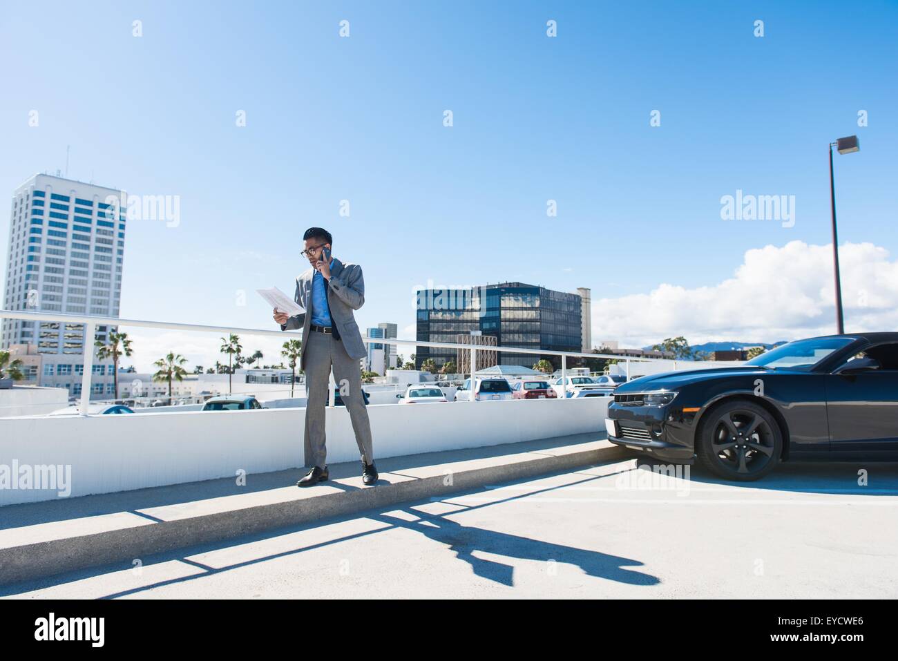 Giovane imprenditore sul tetto della città parcheggio auto in chat sullo smartphone Foto Stock