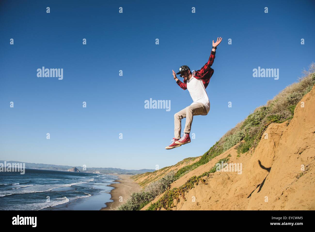 Giovane uomo saltare giù sandy hill, a metà in aria Foto Stock