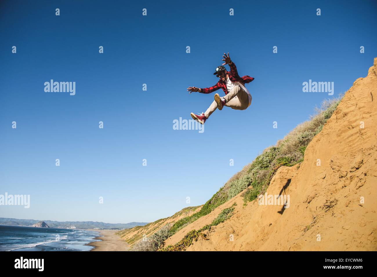 Giovane uomo saltare giù sandy hill, a metà in aria Foto Stock