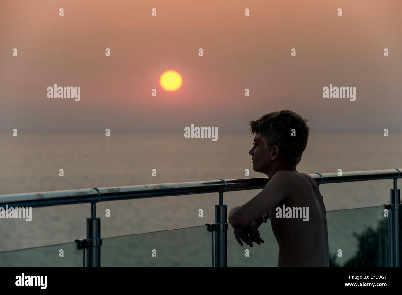 Un ragazzo guarda il sole insieme da una parete di vetro in vacanza Foto Stock