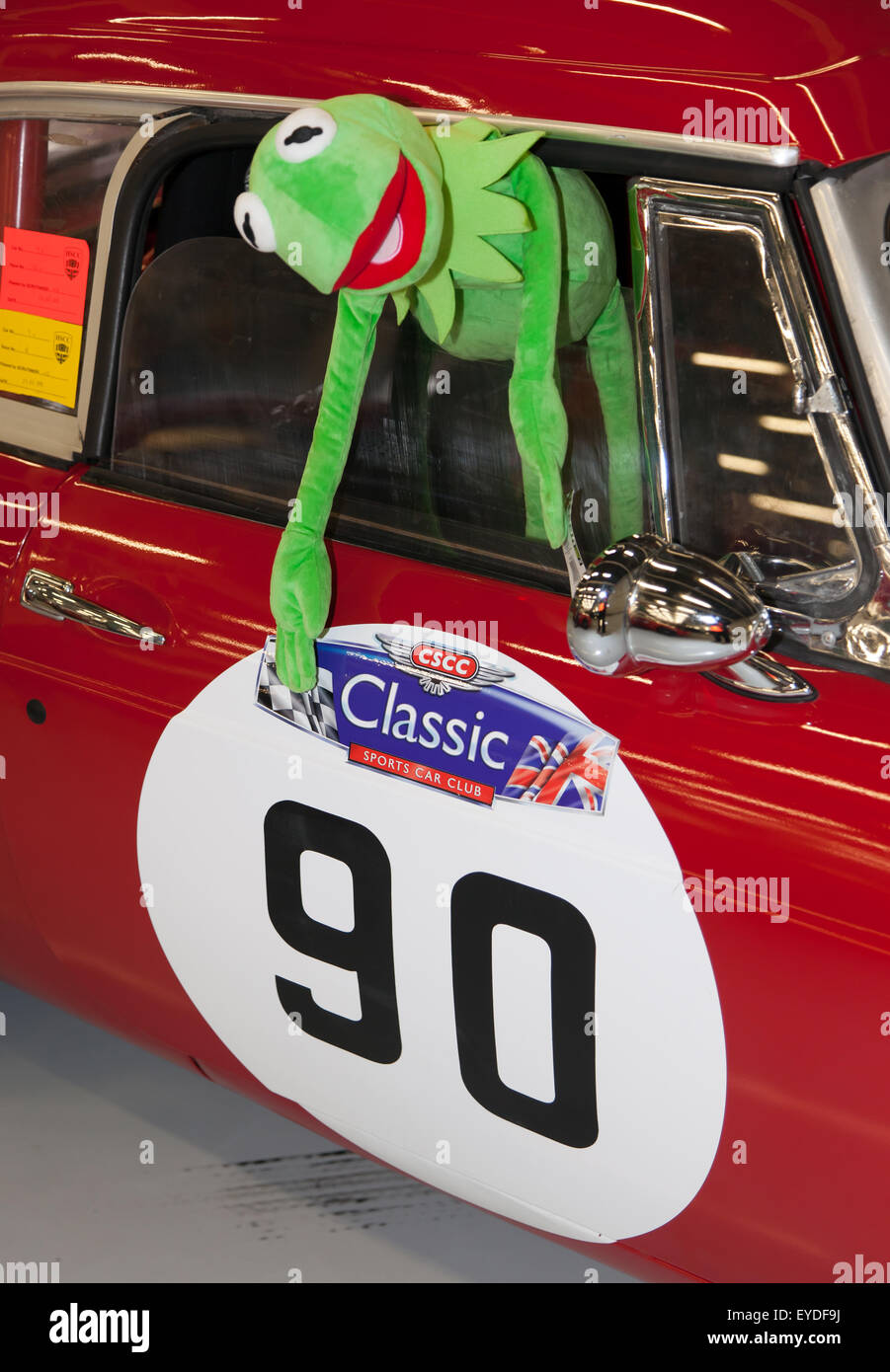 Close-up di un burattino Kermit, puntando a un numero sul lato di un rosso 1963 MGB gara auto nel garage a Silverstone. Foto Stock