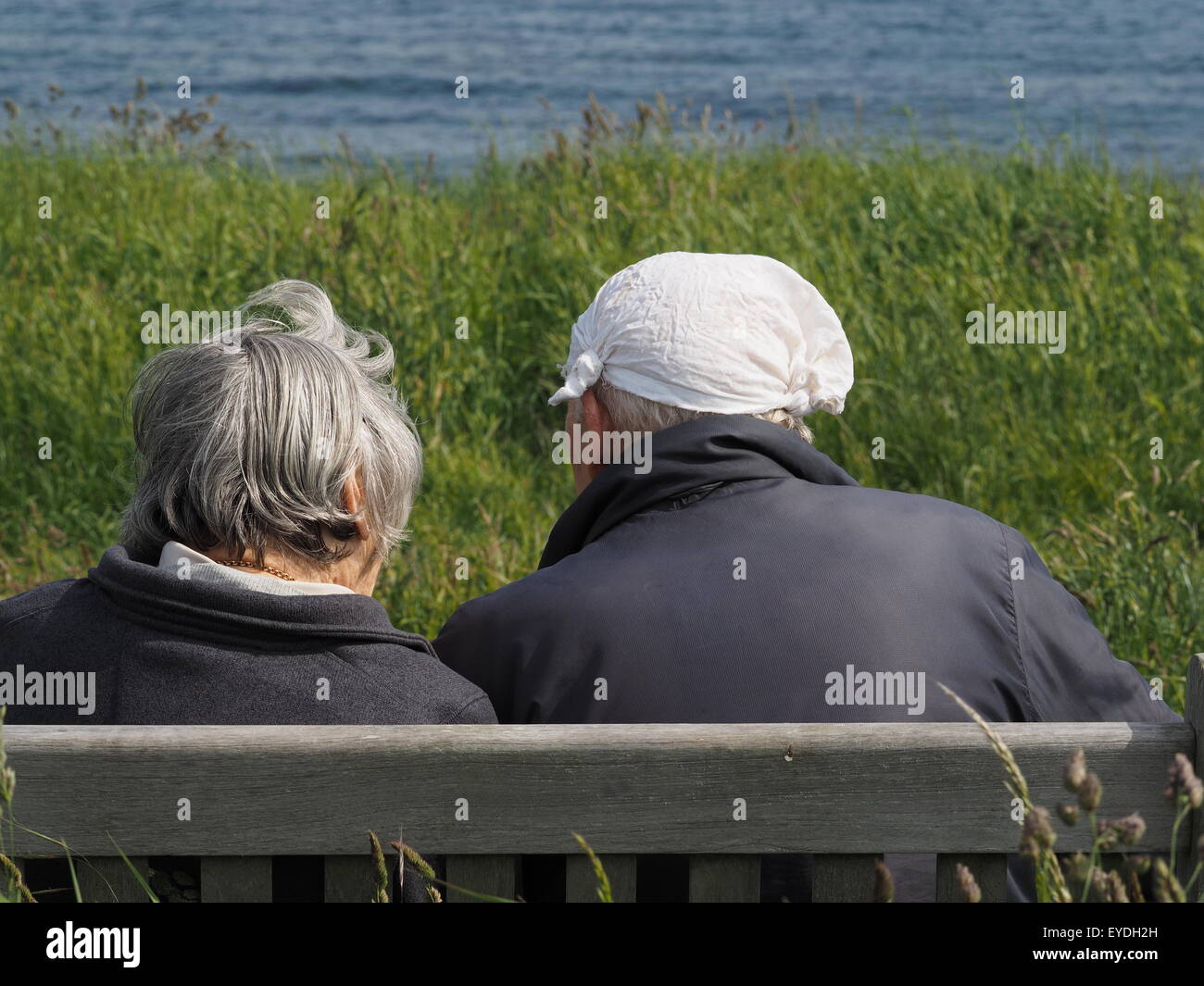 Anonimo companionable coppia di anziani che guarda al mare durante la seduta su una panchina: sta indossando un fazzoletto annodato per un cappello Foto Stock