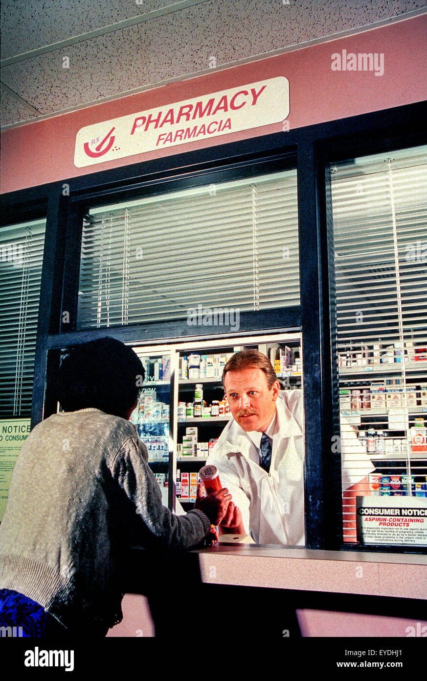 Un addetto consiglia un ispanico un cliente a fare un acquisto presso un Orange, CA, la farmacia ospedaliera. Nota cartello bilingue. Foto Stock