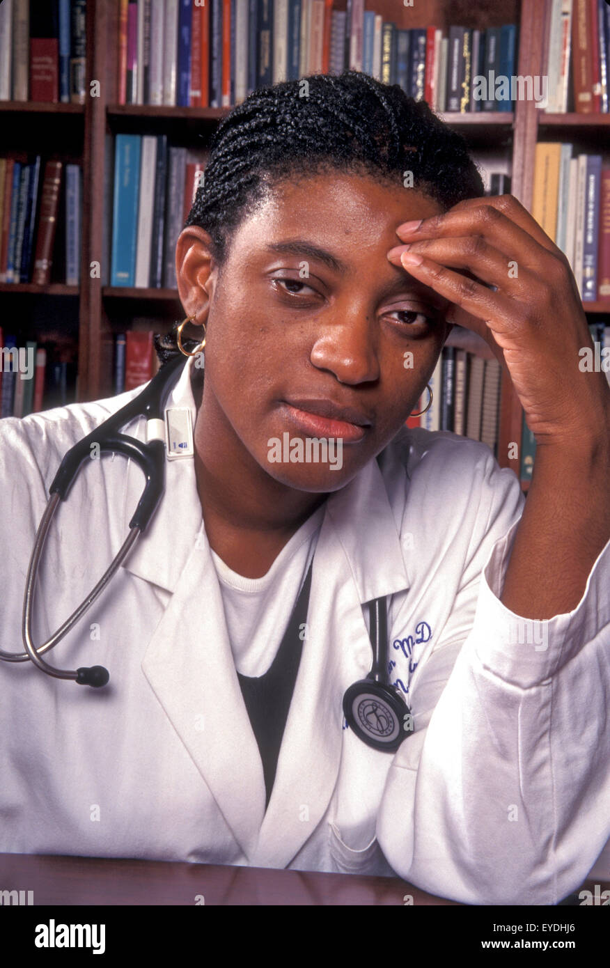 Una stanca americano africano donna medico pone in una Los Angeles Medical Reference Library. Nota lo stetoscopio e il medico tradizionale del rivestimento bianco. Foto Stock