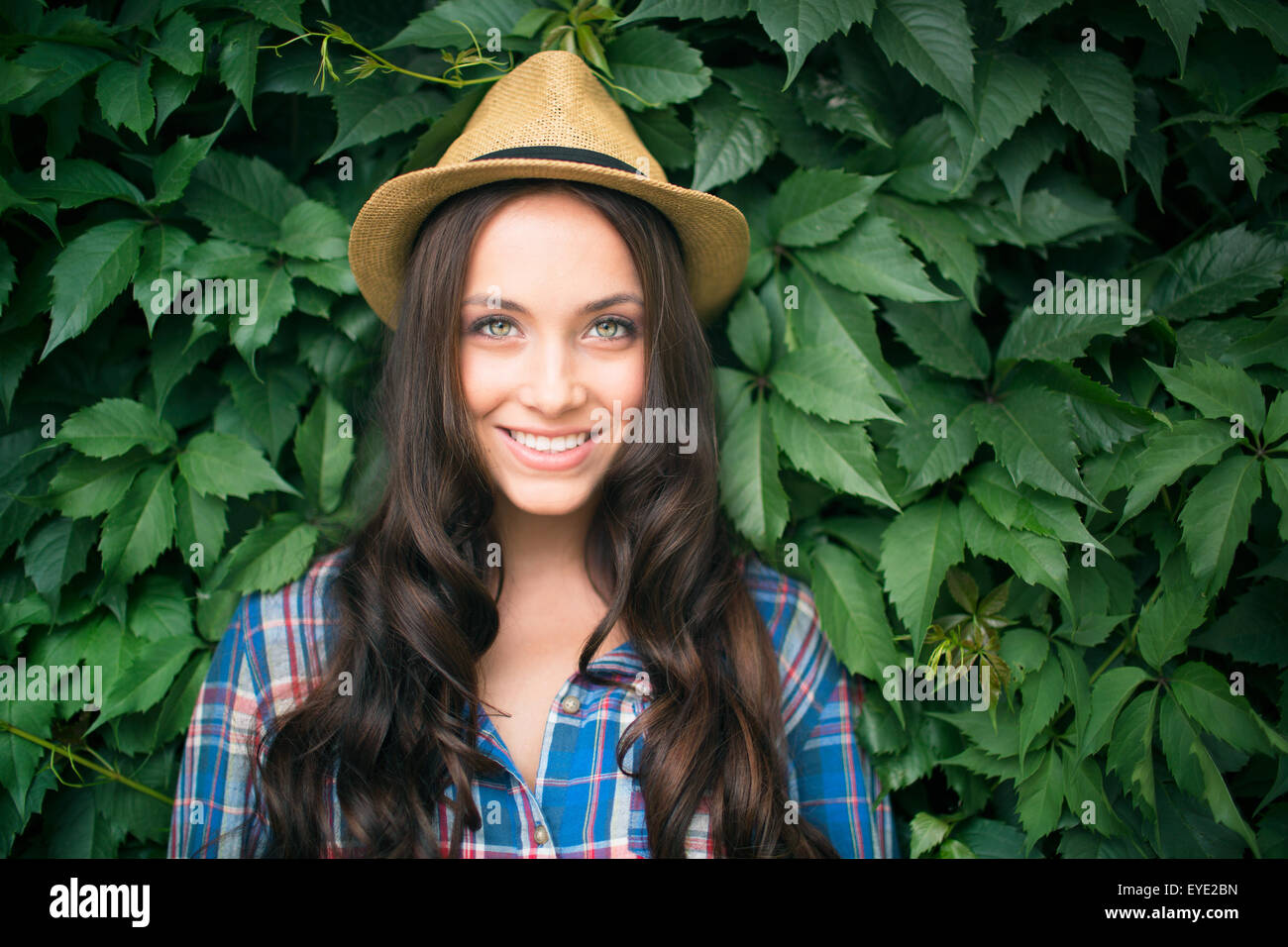 Felice femmina in cowgirl hat e shirt guardando la fotocamera dalla pianta verde Foto Stock