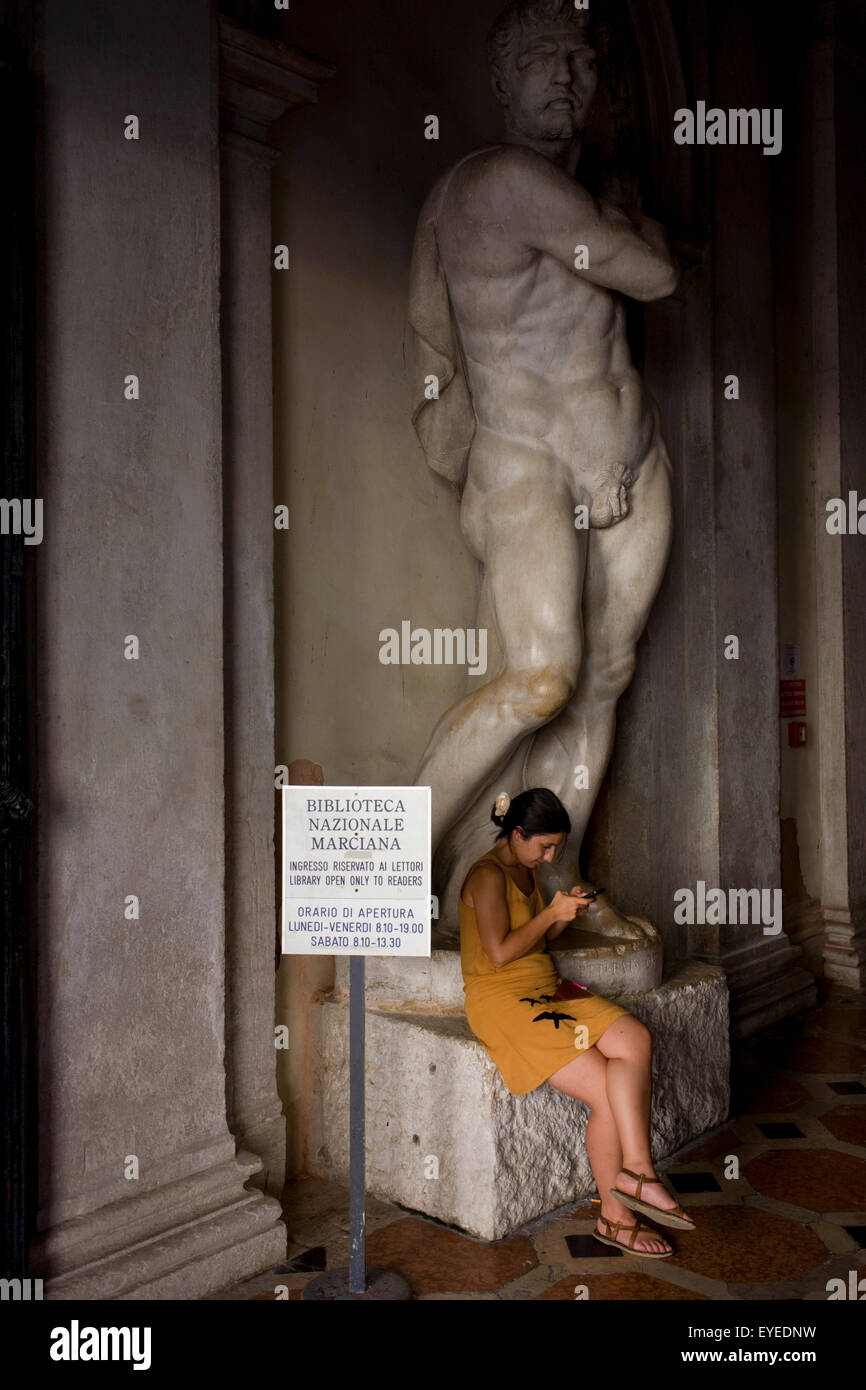 Ragazza controlla messaggi fuori l'ingresso della Biblioteca Nazionale Marciana in coperta Procuratie Nuovo di Piazza San Mar Foto Stock