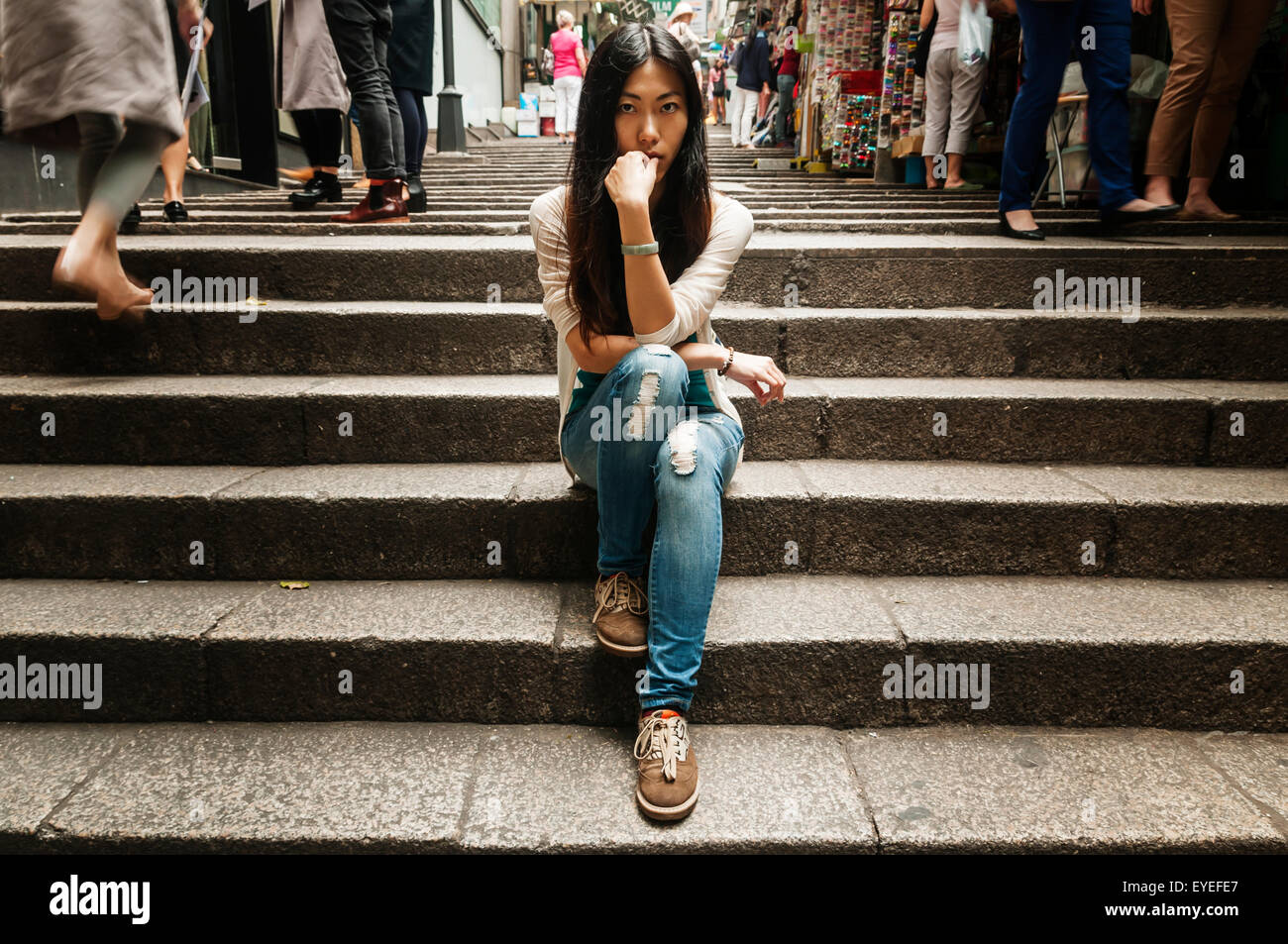 Il cinese giovane donna in posa sui passi vicino a Hollywood Street, occupato persone che passano intorno a lei; Hong Kong, Cina Foto Stock